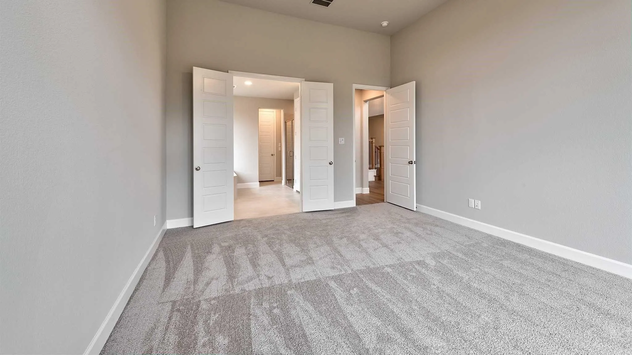 Spacious room featuring neutral carpeting, light-toned walls, and multiple panel doors