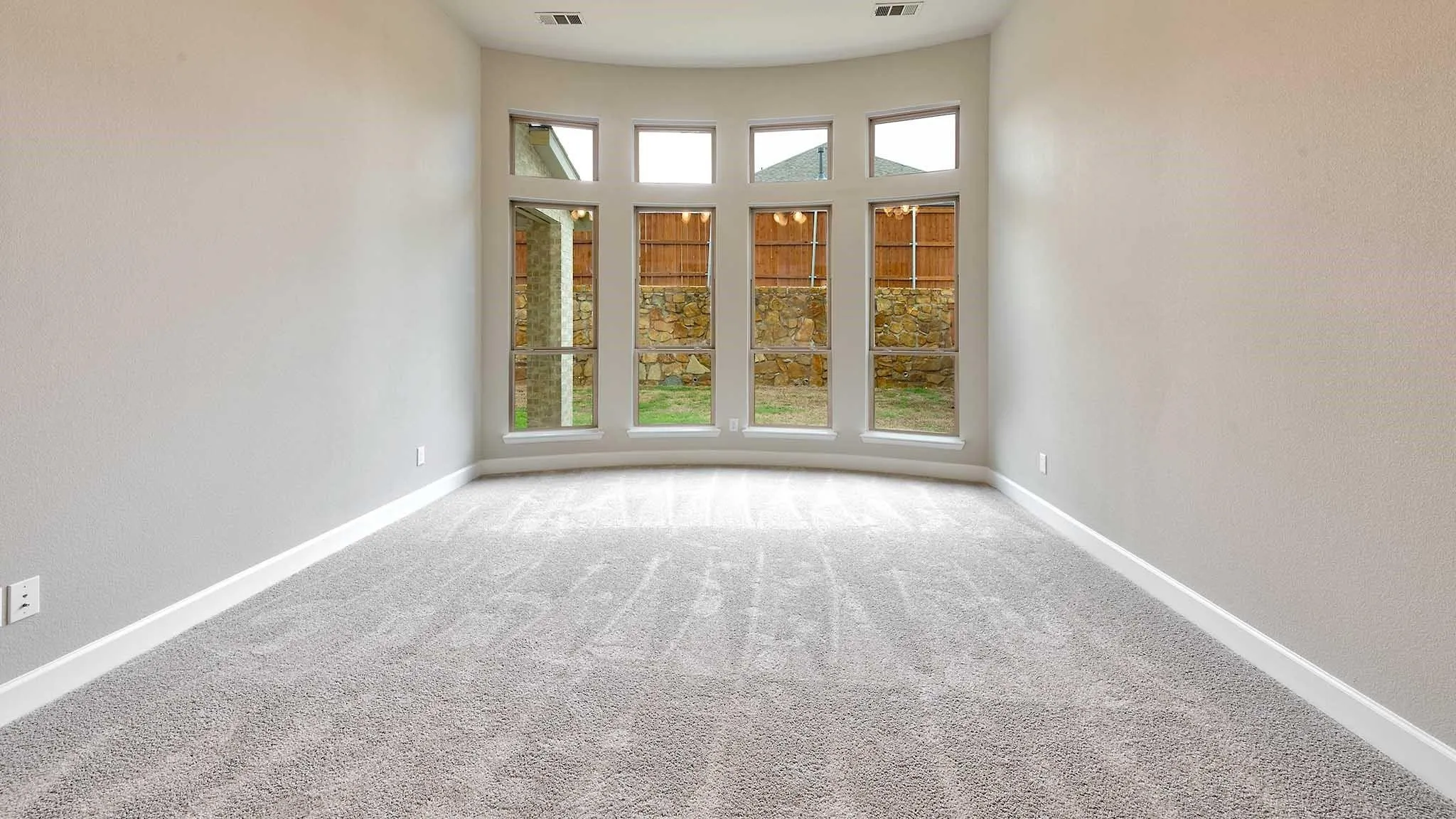 Curved window wall with multiple panes and transom windows, light gray carpeting, and neutral wall tones