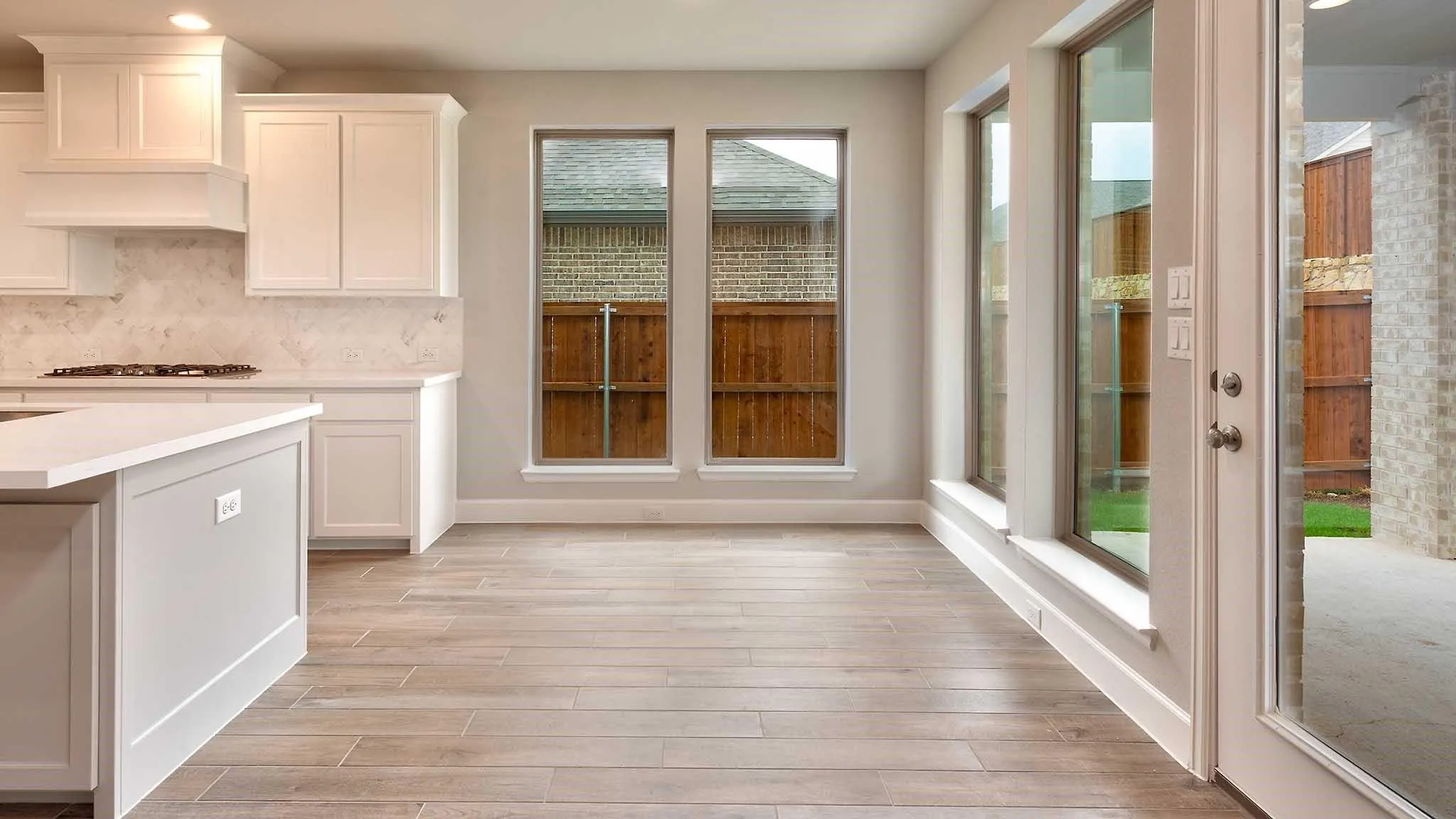 Open-concept area featuring wood-finish flooring, white cabinetry, a kitchen island with a light-toned countertop, and multiple large windows