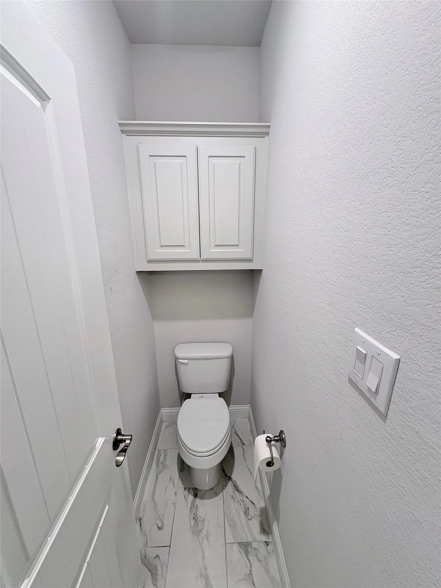 Built-in white cabinetry, modern toilet, and white-veined floor tiling