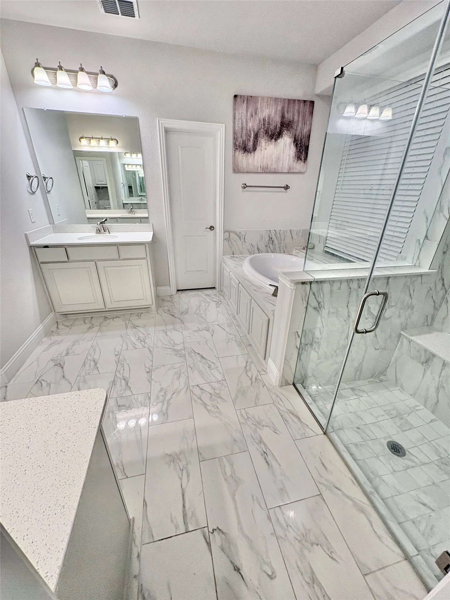White cabinetry with light-toned countertop, large vanity mirror, and a built-in soaking tub with a tiled surround