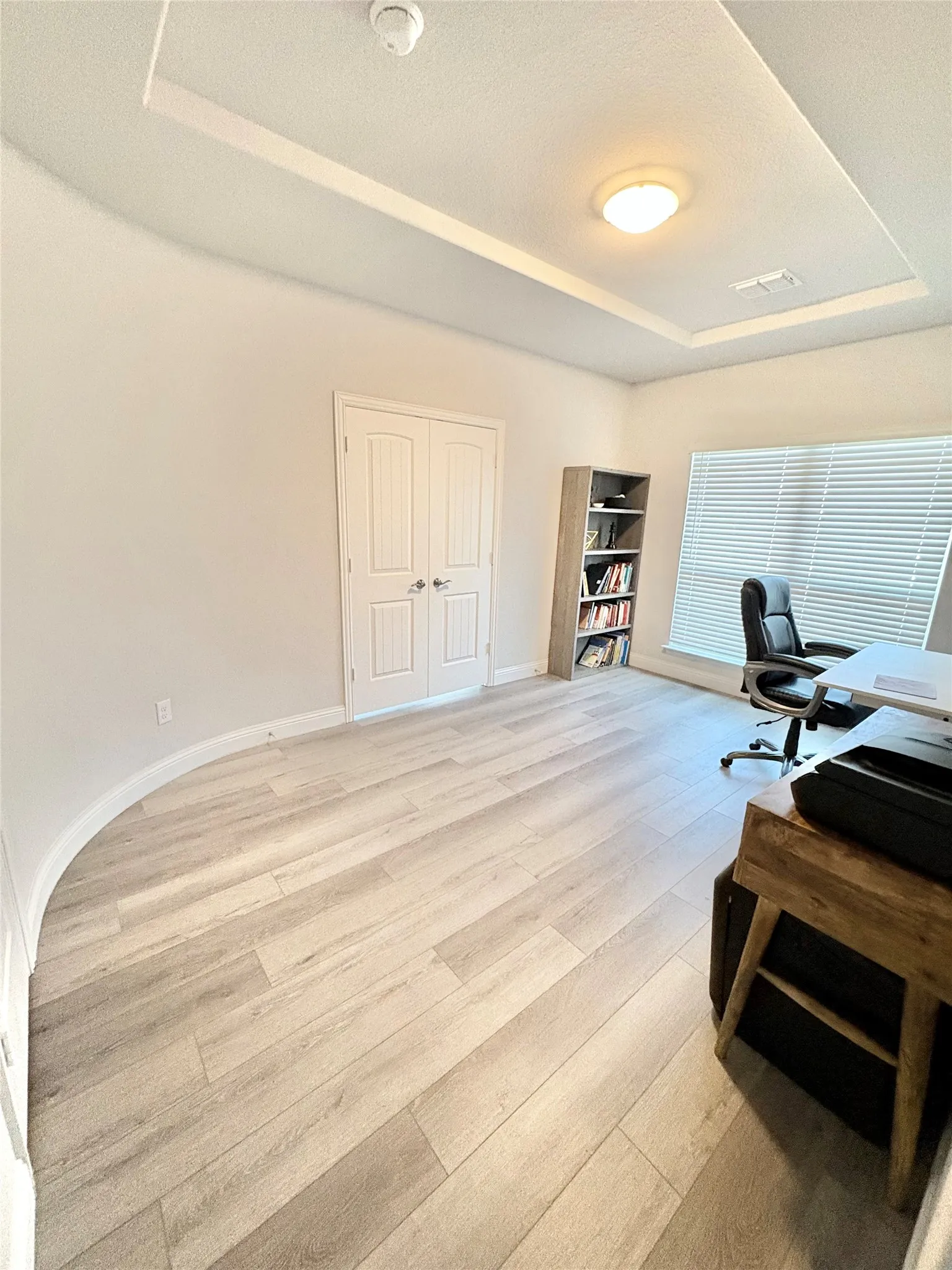 Wood-finish flooring, tray ceiling, flush mount lighting, and double panel doors