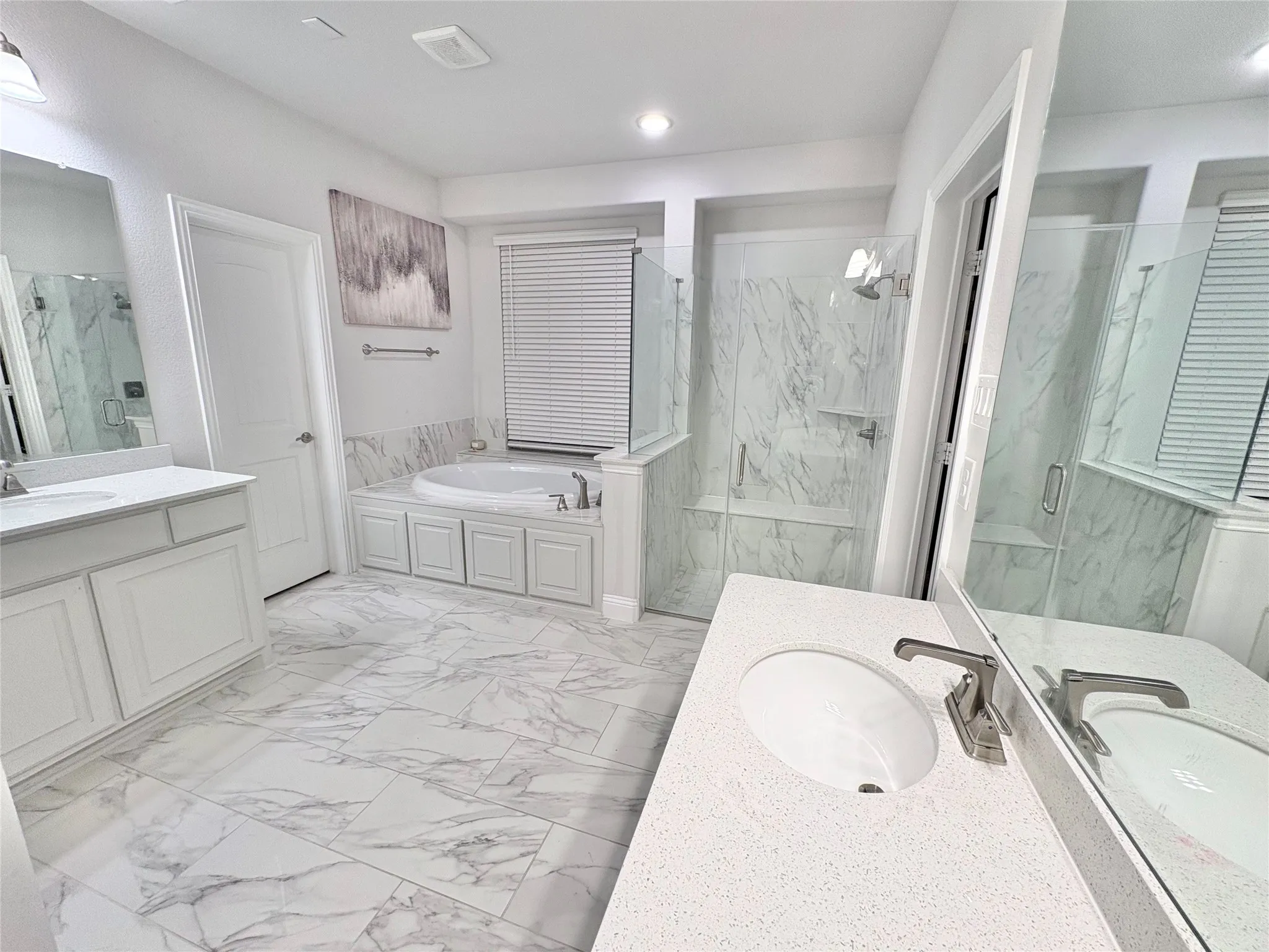 Freestanding soaking tub, glass-enclosed shower, dual vanity with undermount sinks, quartz countertops, and large format marble-look tile flooring