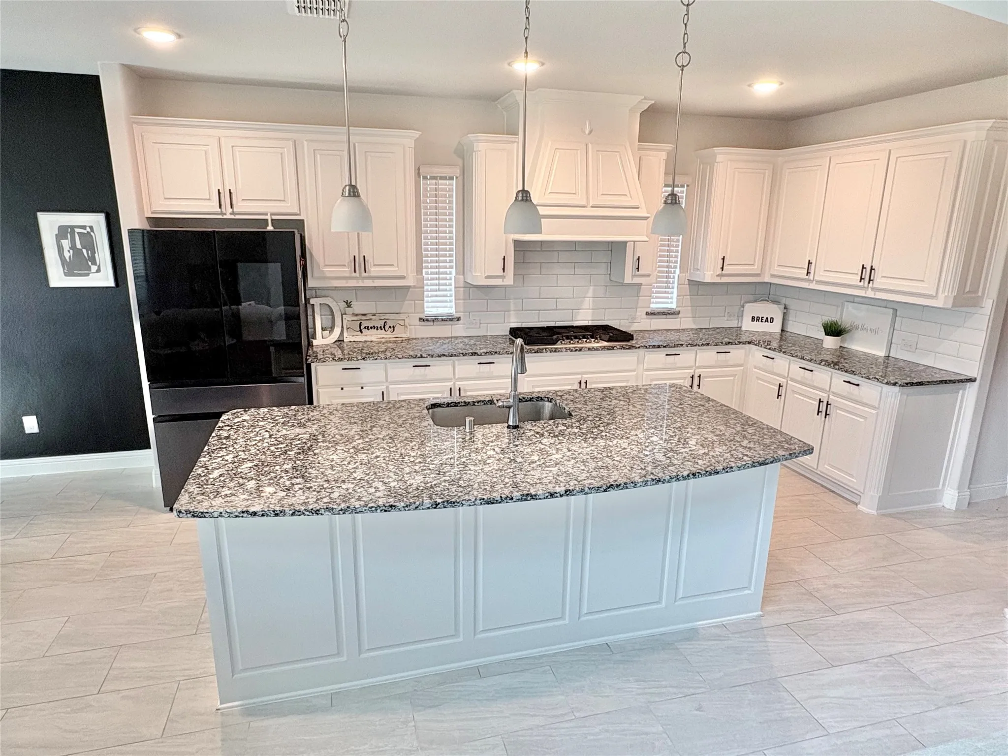 Kitchen featuring white cabinetry, granite countertops, subway tile backsplash, a center island with sink, and pendant lighting