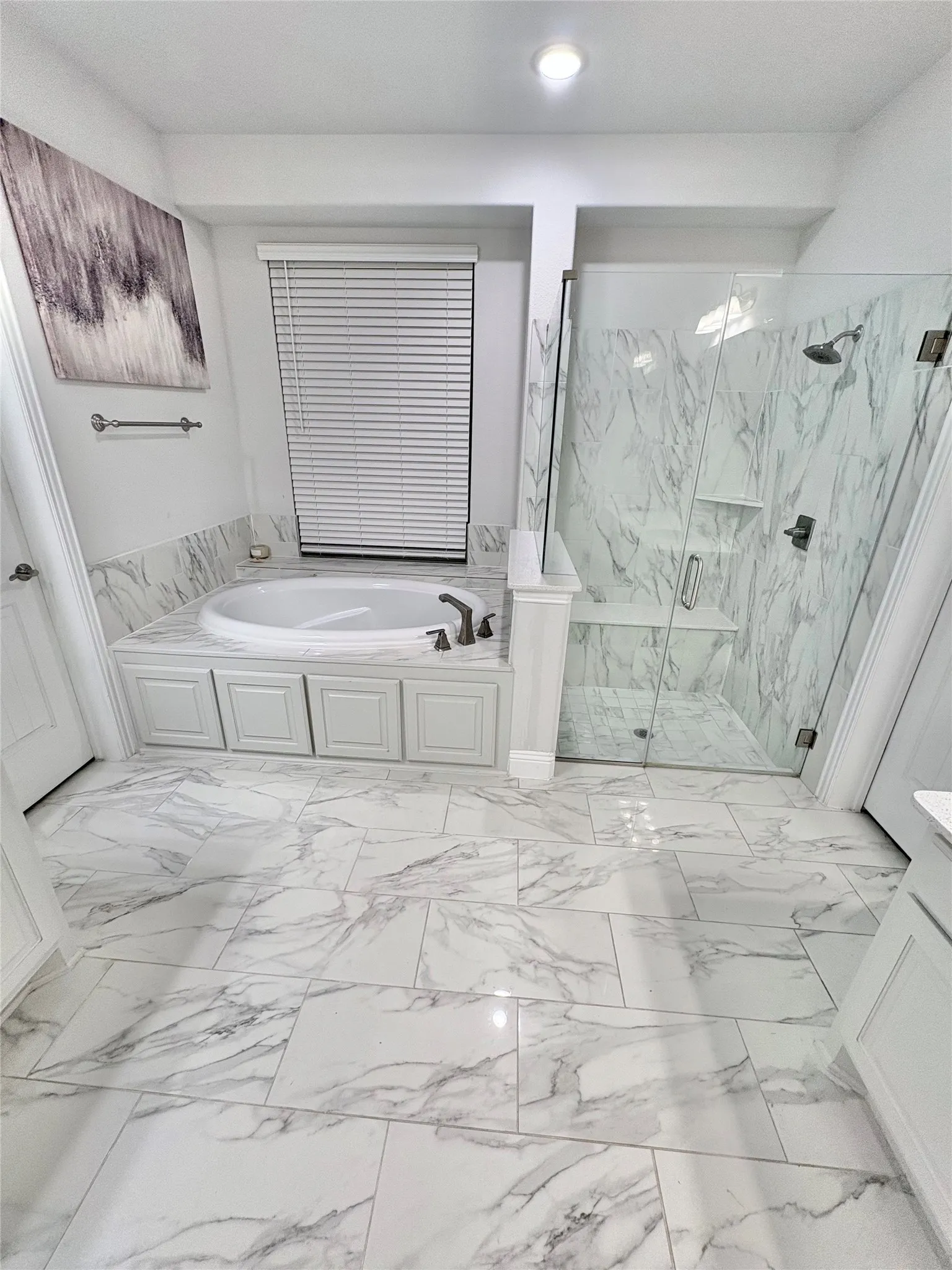 Built-in soaking tub with paneled base, walk-in shower with glass enclosure, white tile flooring with veining, recessed lighting, and a window with blinds