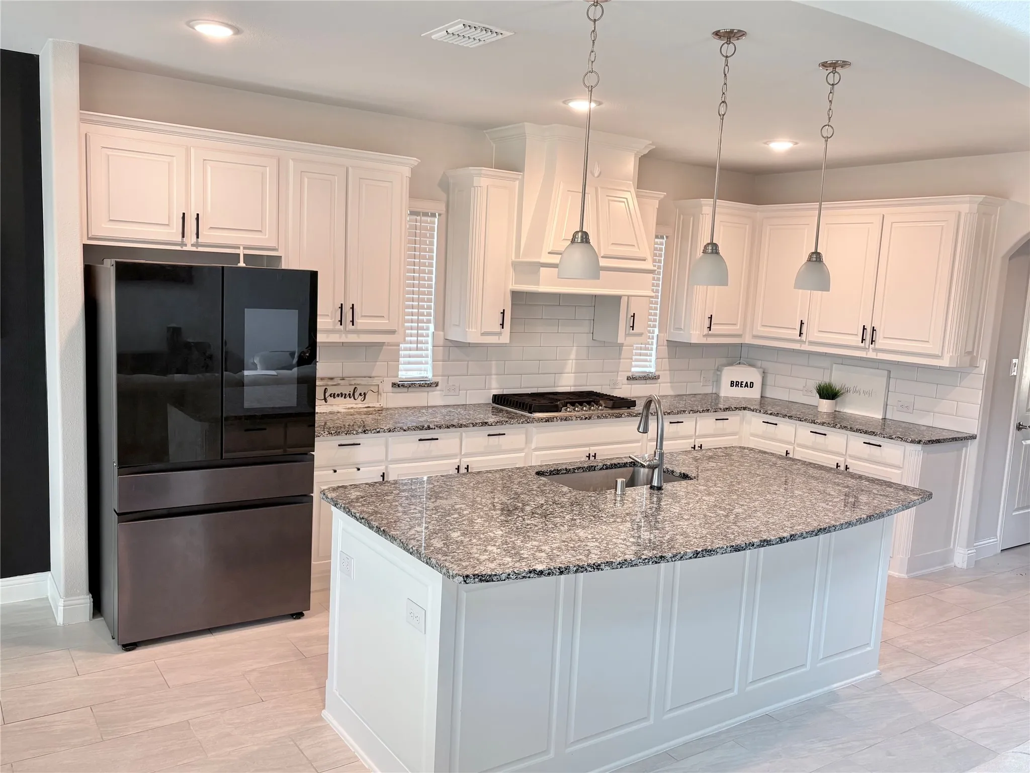 White cabinetry with crown molding, granite countertops, subway tile backsplash, stainless steel refrigerator, and recessed lighting