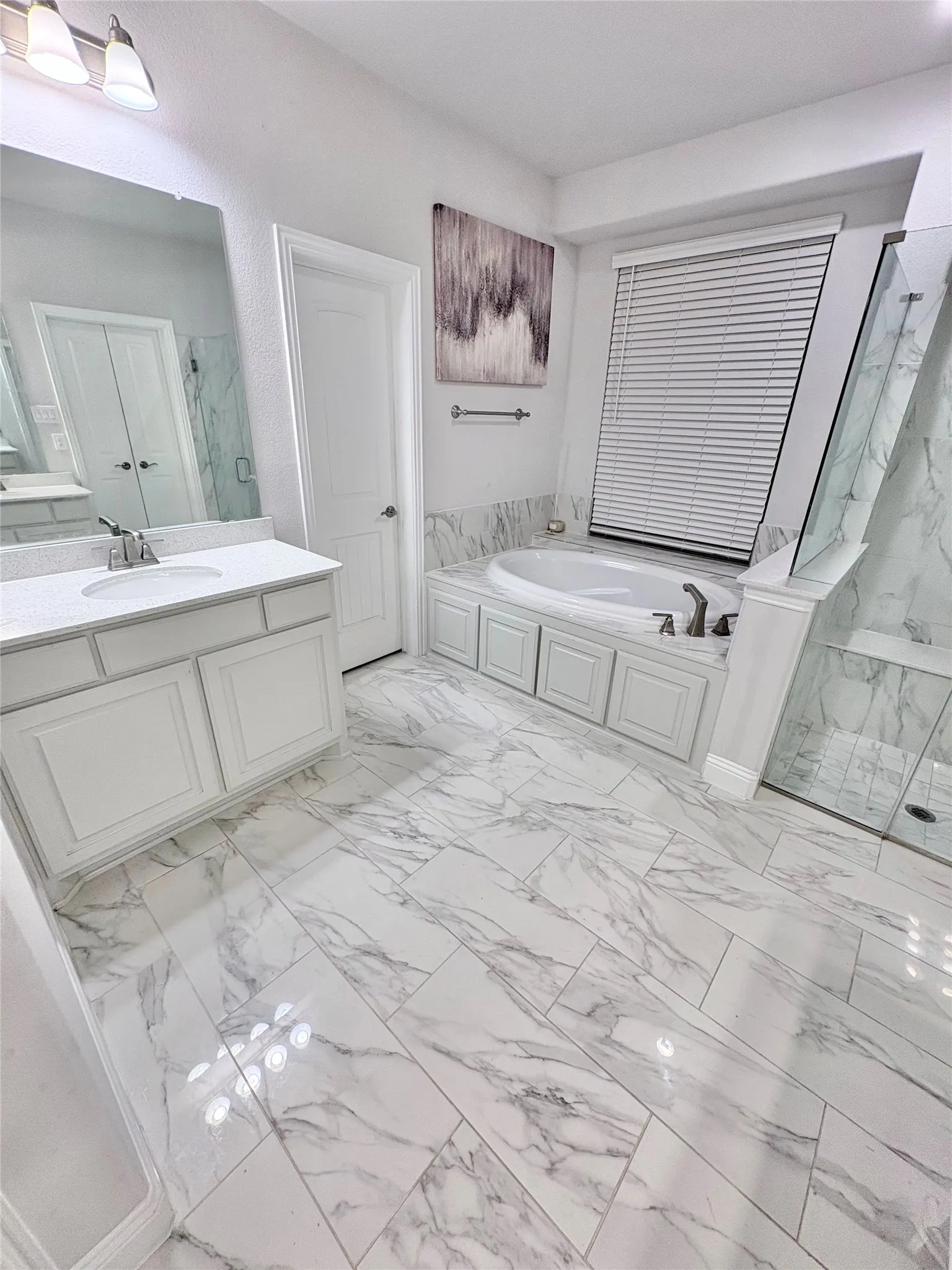 White marble-look tile flooring, white vanity with quartz countertop and undermount sink, built-in bathtub with tiled surround, and glass-enclosed shower
