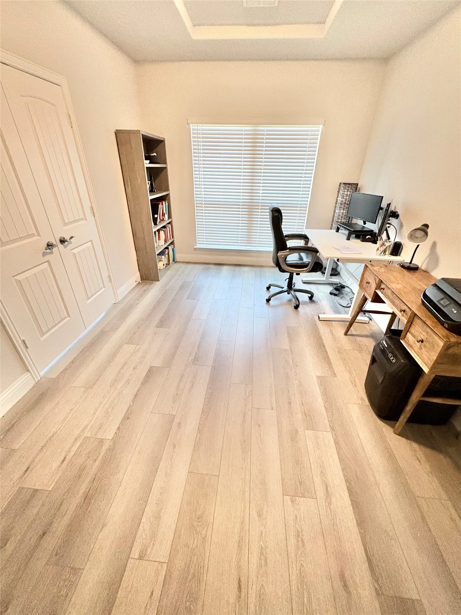 Wood-finish flooring, white paneled door, and a prominent window with blinds