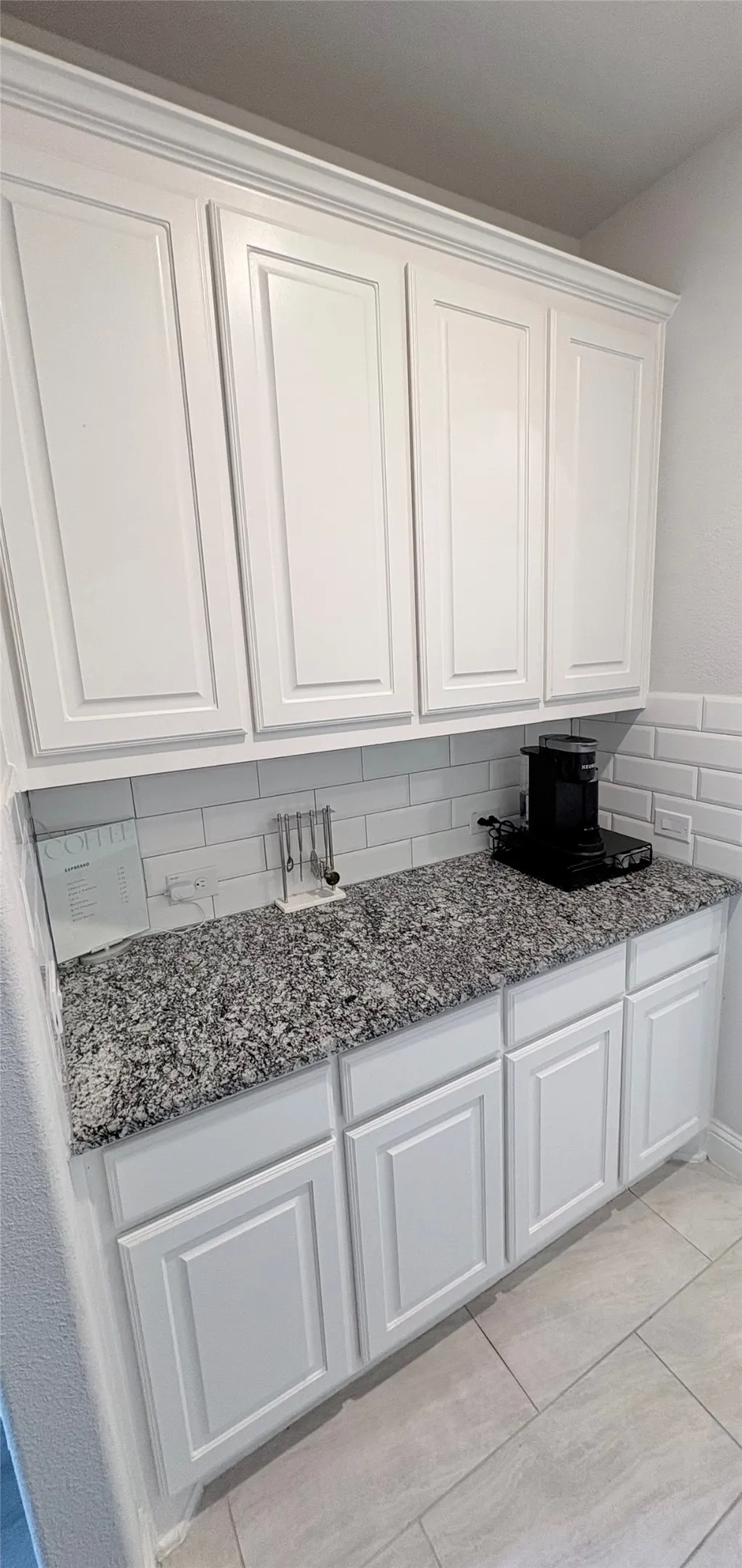 White shaker-style cabinetry with crown molding, granite-finish countertops, white subway tile backsplash, and light-toned tile flooring