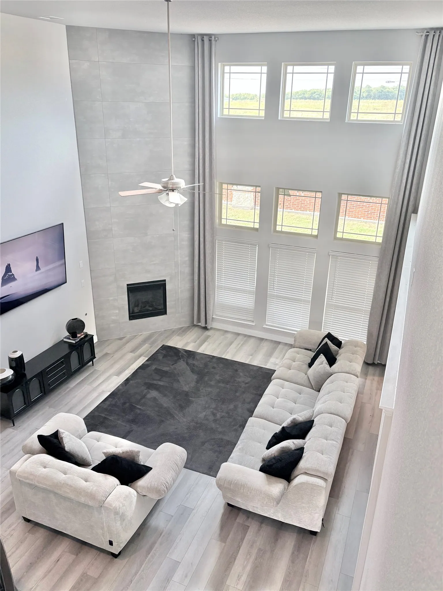 Living space featuring a two-story ceiling, multiple windows, a ceiling fan, a fireplace, and wood-finish flooring