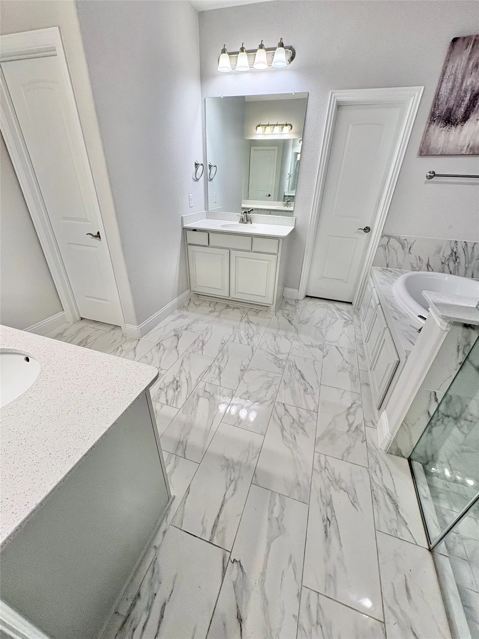 Dual vanity sinks, marble-look floor tiling, built-in bathtub, glass-enclosed shower, and built-in cabinetry