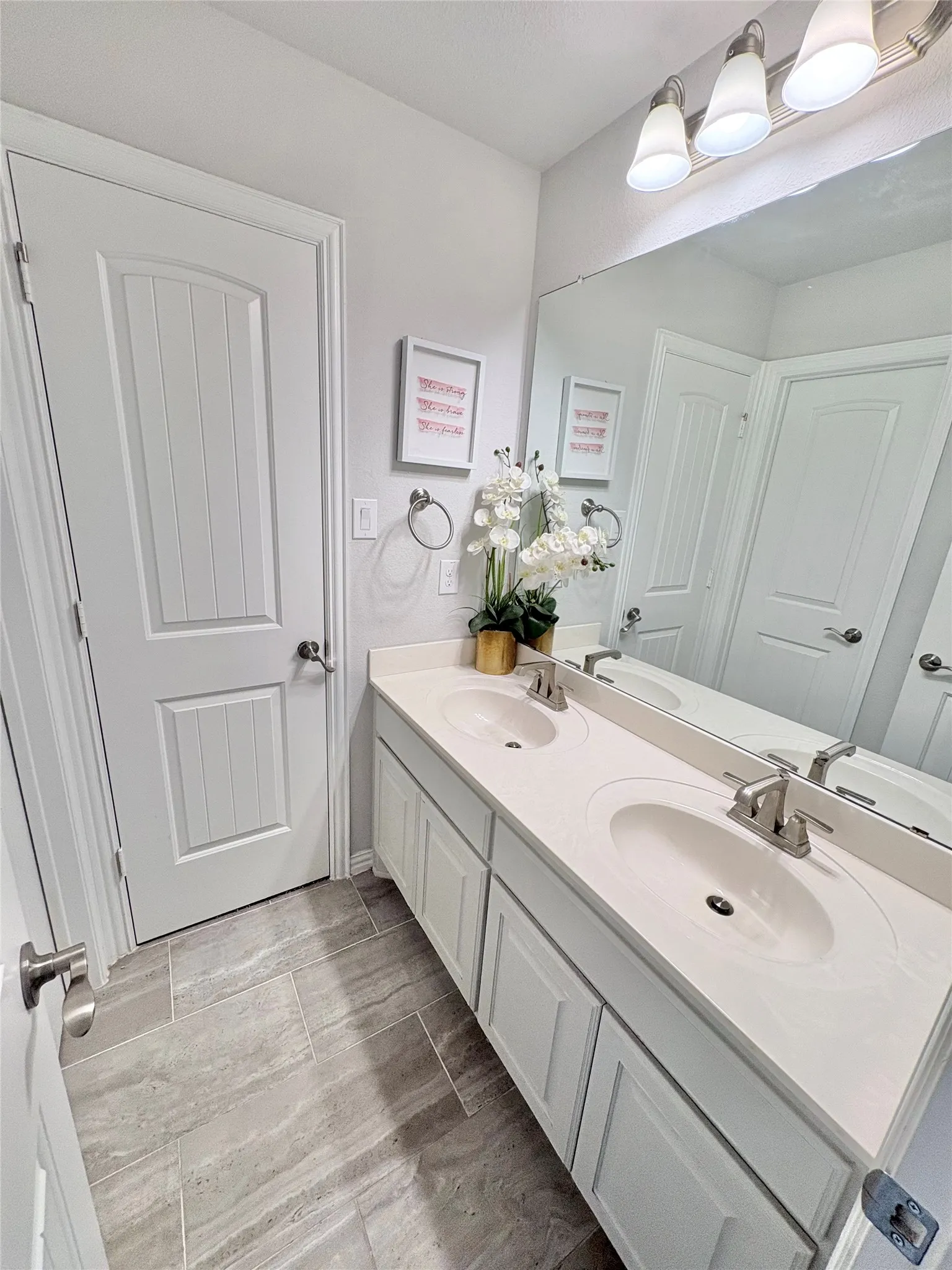 Dual vanity with integrated sinks and brushed nickel faucets, undermount cabinetry, full-width mirror, and tile flooring