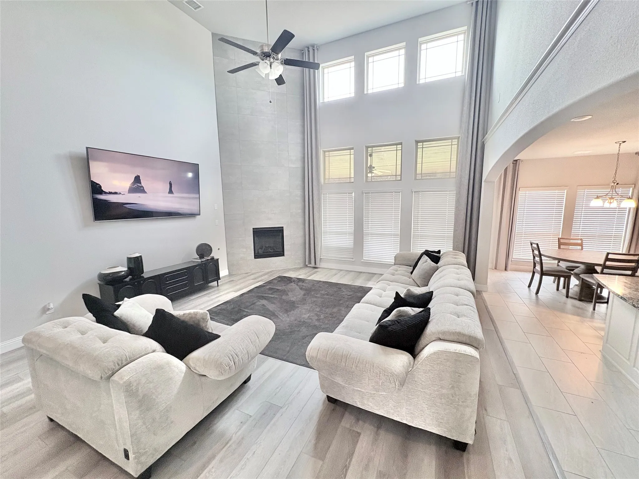 Two-story ceiling, large format tile flooring, modern fireplace, high windows with blinds, and an arched entryway