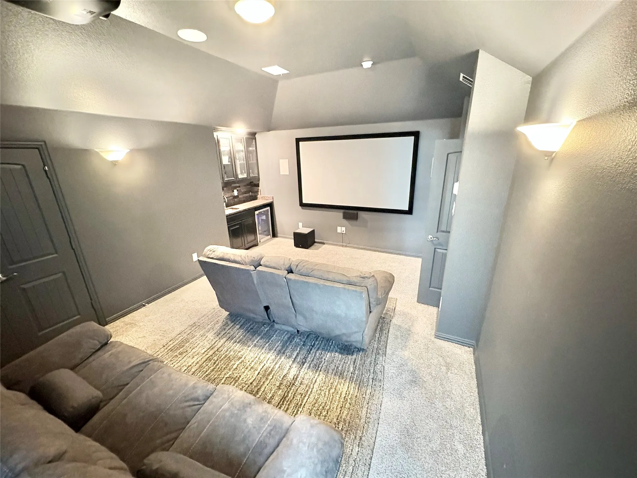 Dedicated entertainment room featuring a large projection screen, built-in wet bar, recessed lighting, and wall sconces
