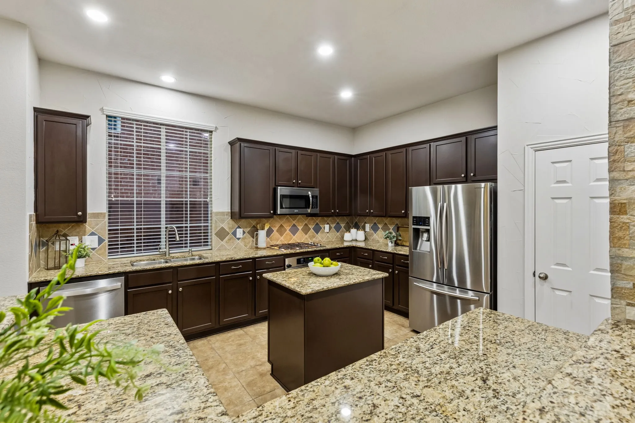 Kitchen featuring dark wood cabinetry, granite countertops, stainless steel appliances, a tiled backsplash, and recessed lighting