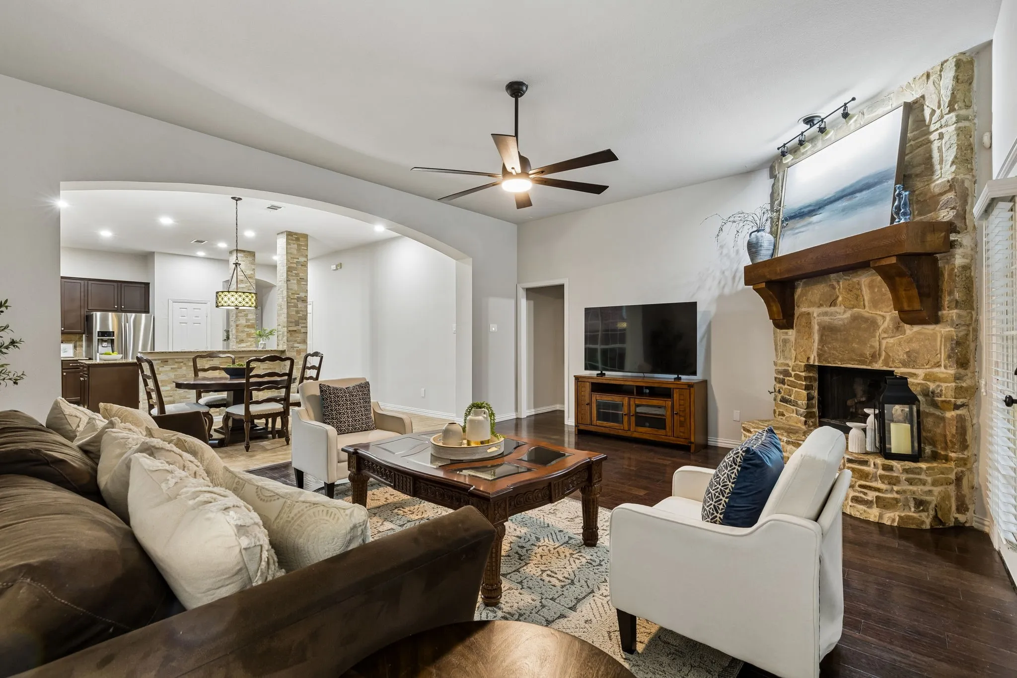 Stone-clad fireplace with wood mantel, dark wood-finish flooring, recessed lighting, and a ceiling fan