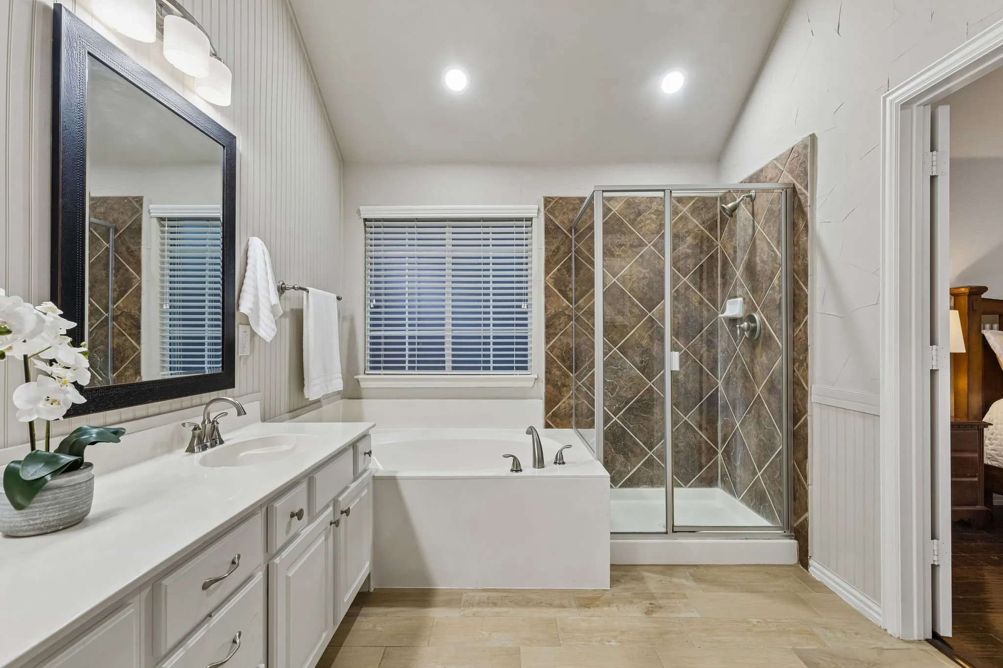 Dual vanity with light-colored countertop, built-in soaking tub, and enclosed shower with tiled surround
