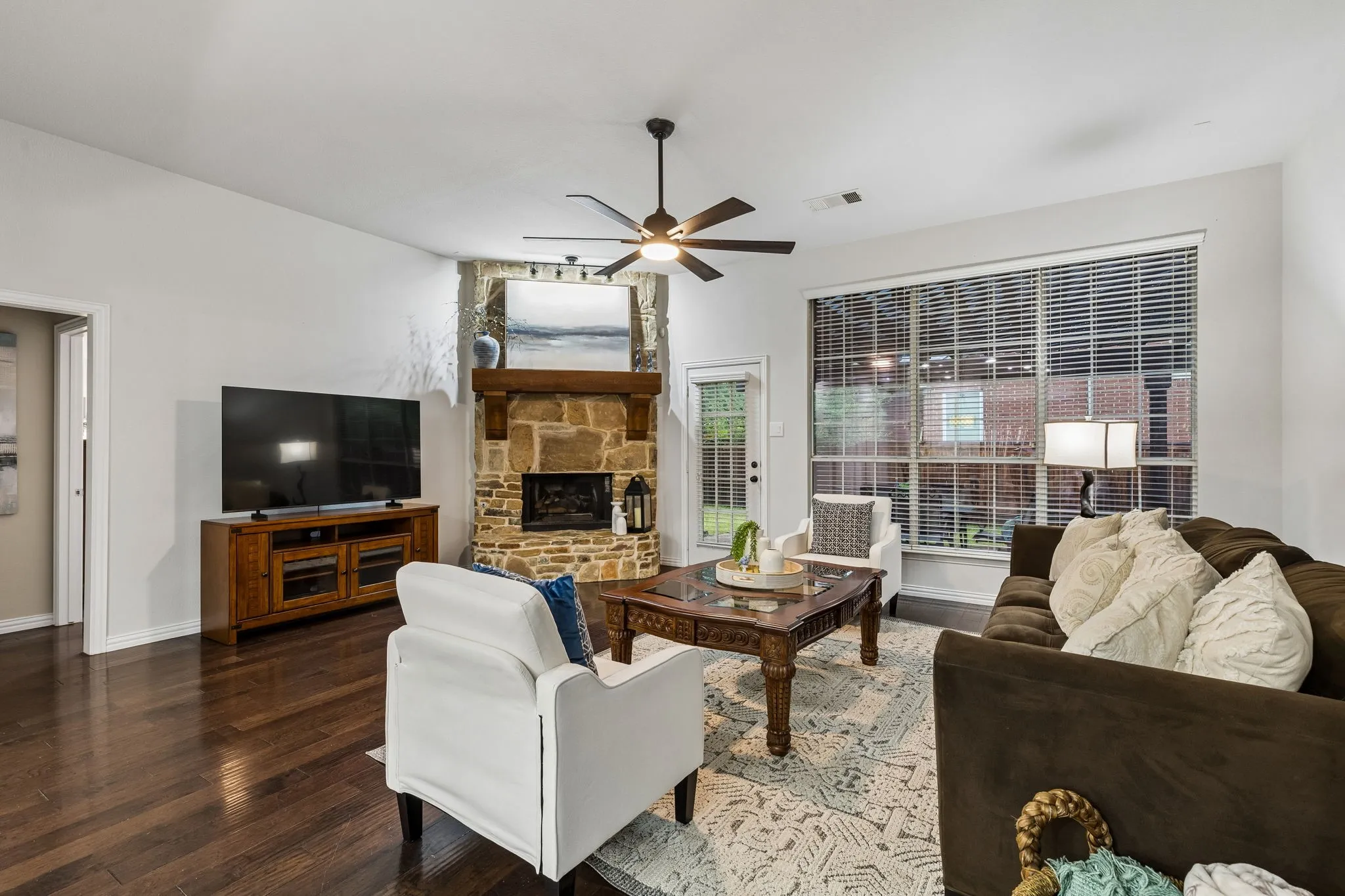 Stone-faced fireplace with a substantial wood mantel, wood-finish flooring, and a ceiling fan