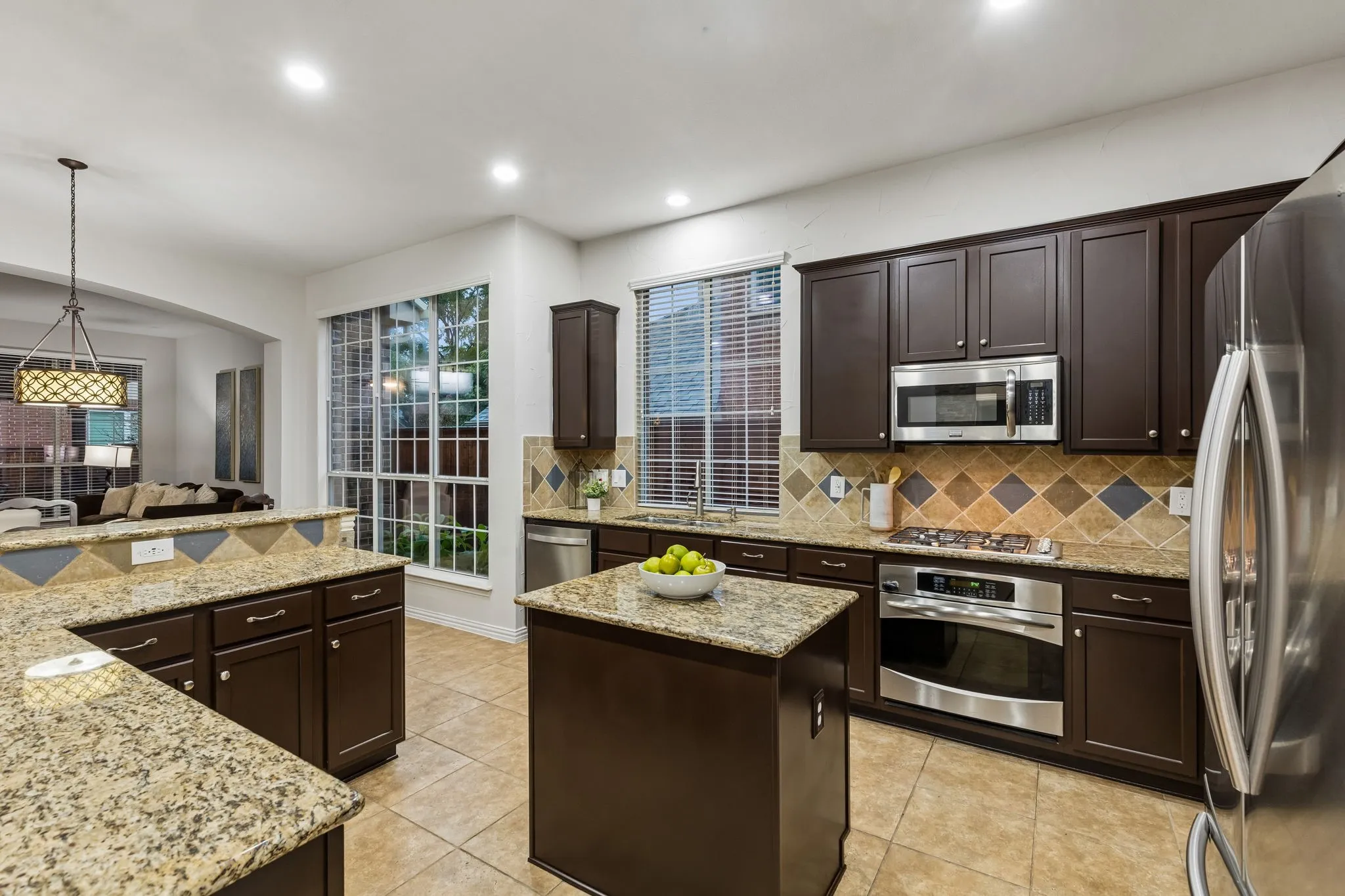 Kitchen featuring dark wood cabinetry, light-toned countertops, a central island, stainless steel appliances, and a tiled backsplash