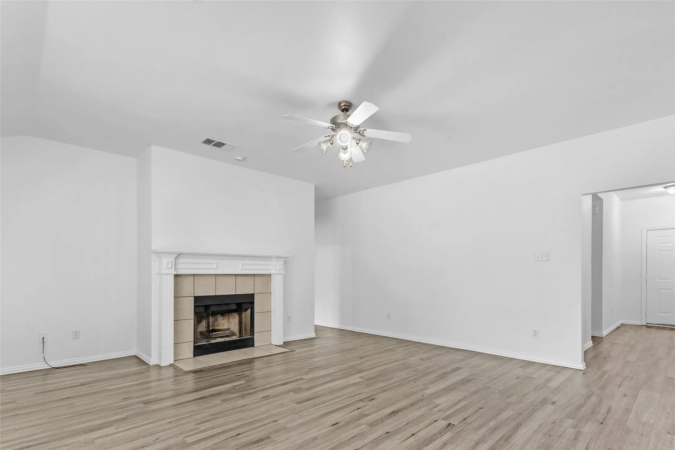 Living room with tiled wood-burning fireplace, sloped ceiling, and wood-look floors