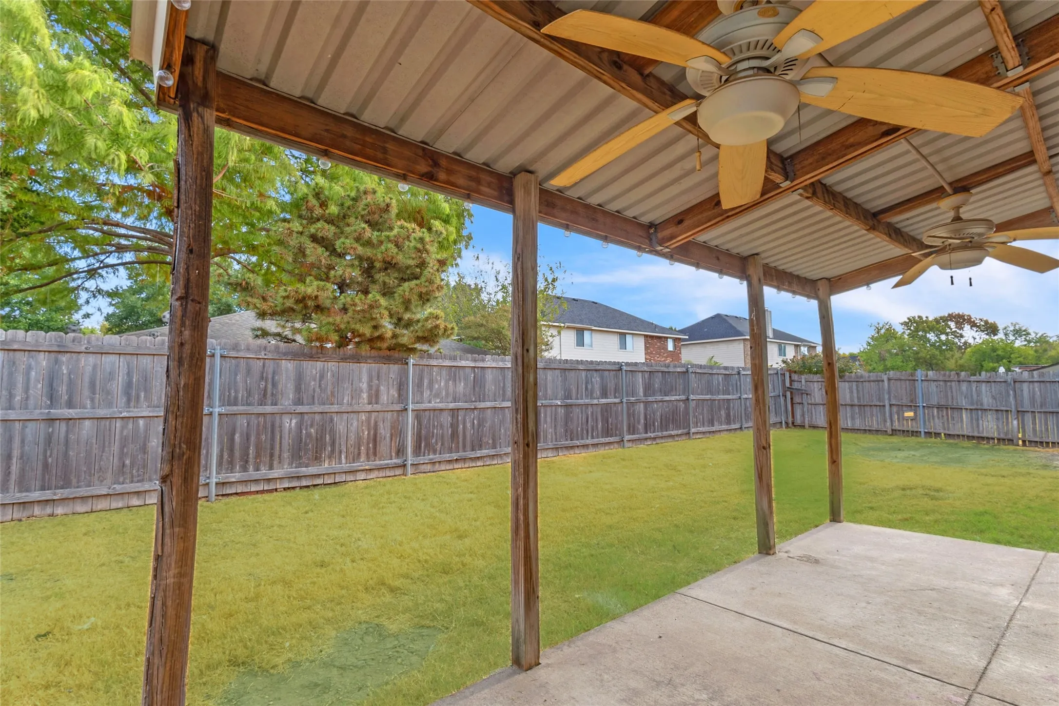 Covered patio with two ceiling fans overlooking the fenced backyard of this Crandall TX home