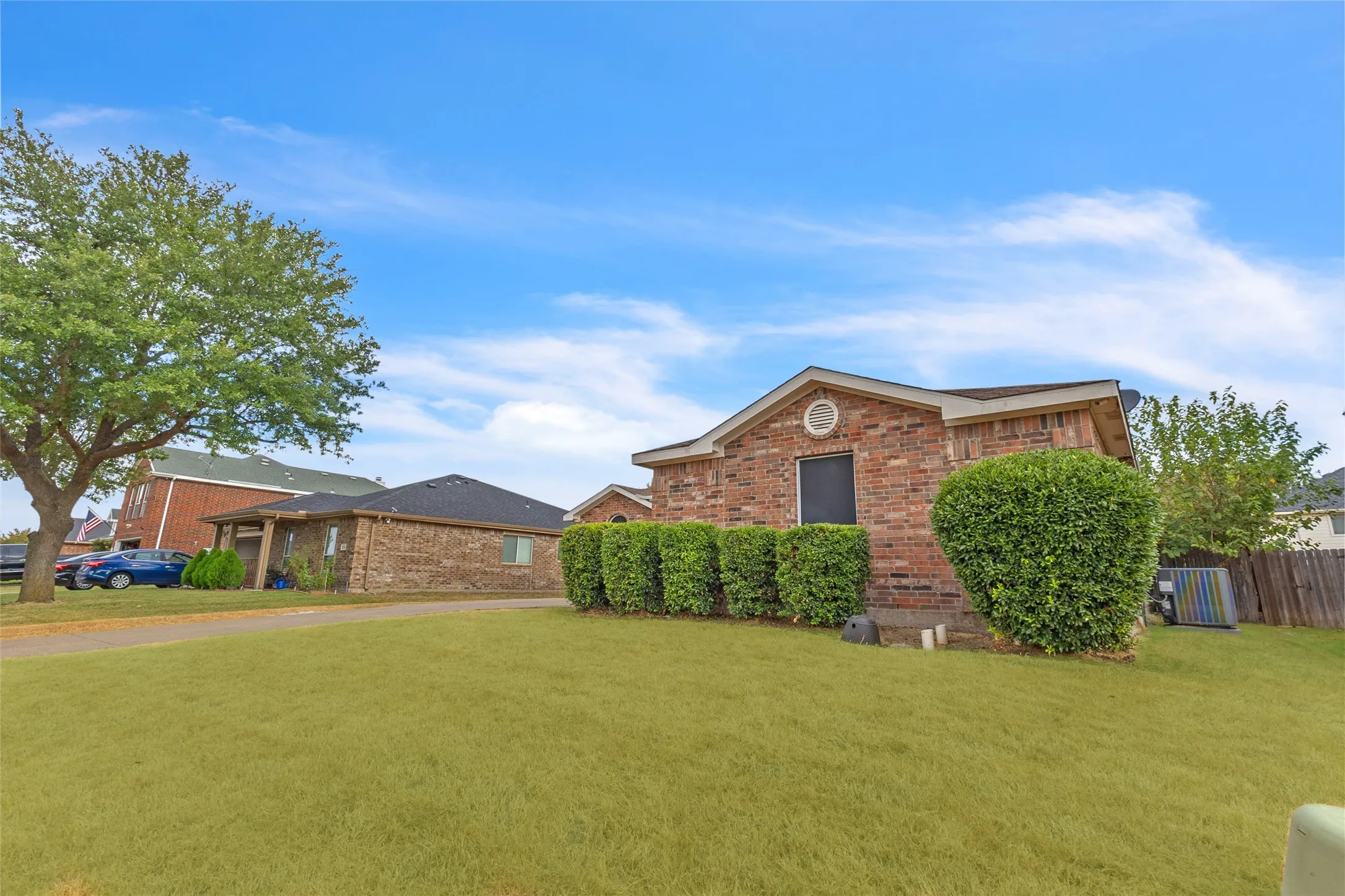 Side view of the brick exterior with trimmed hedges and a broad front lawn