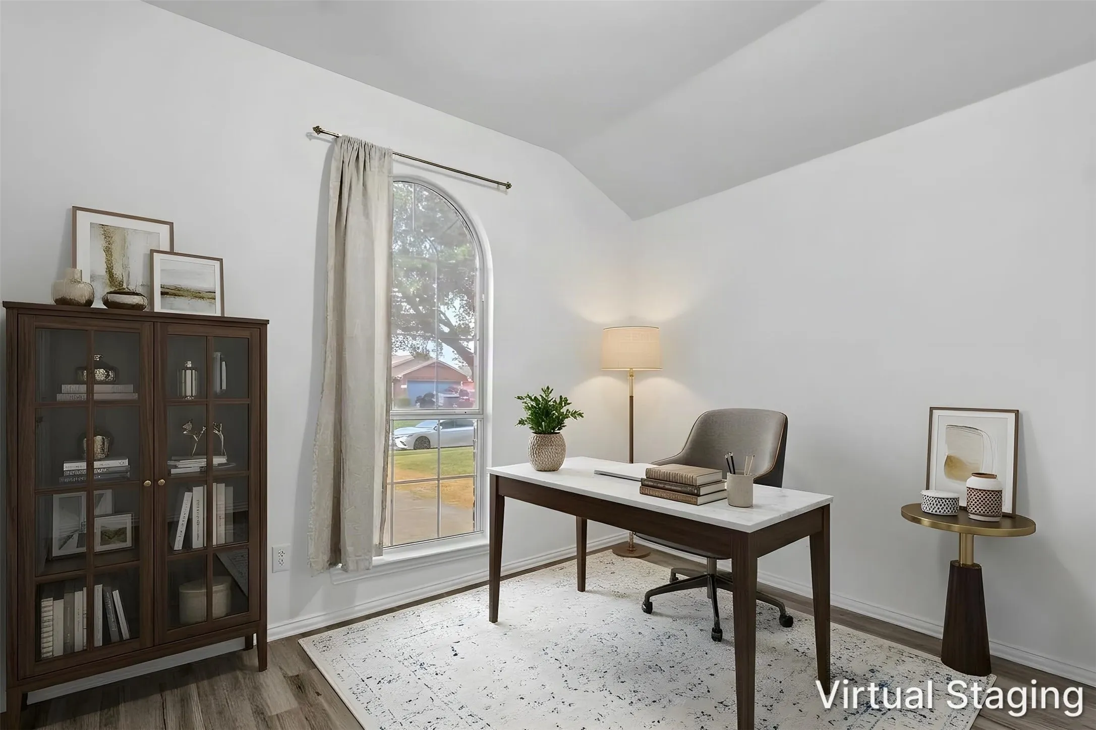 Virtually staged home office with vaulted ceiling and a tall arched window facing the front yard