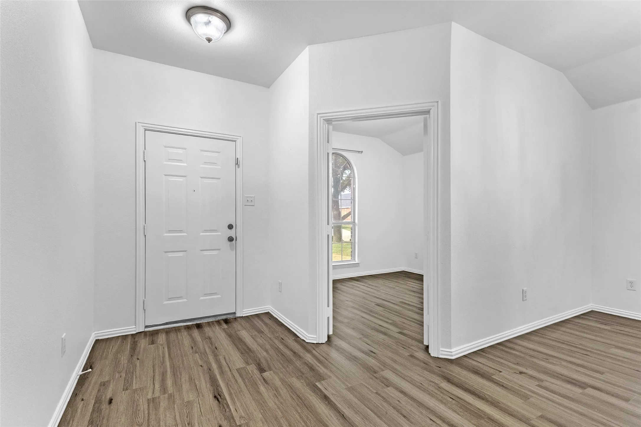Entry foyer with wood-look floors and a view into the front office with its tall arched window