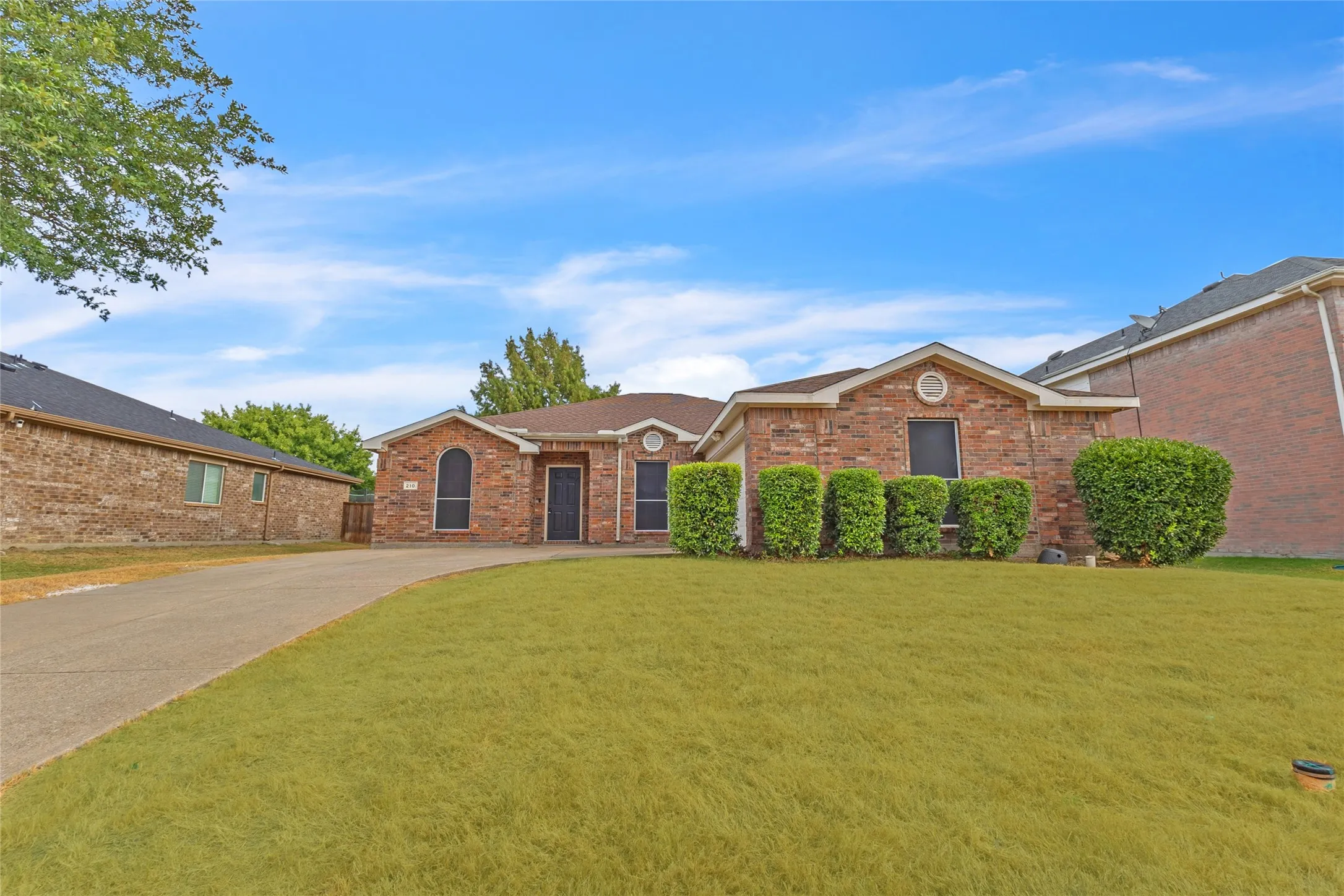 Front yard with mature trees, trimmed shrubs, and a curved driveway at this River Ridge home