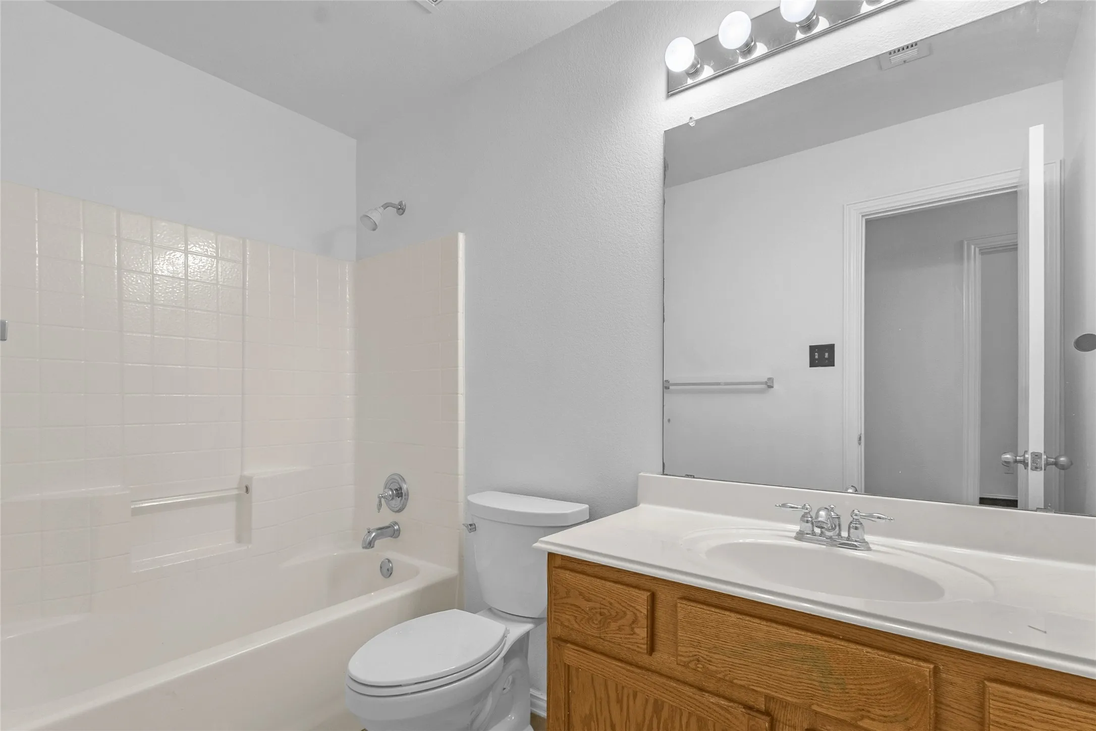 Full hall bath with tub-shower combo, tile surround, and a wood-tone vanity