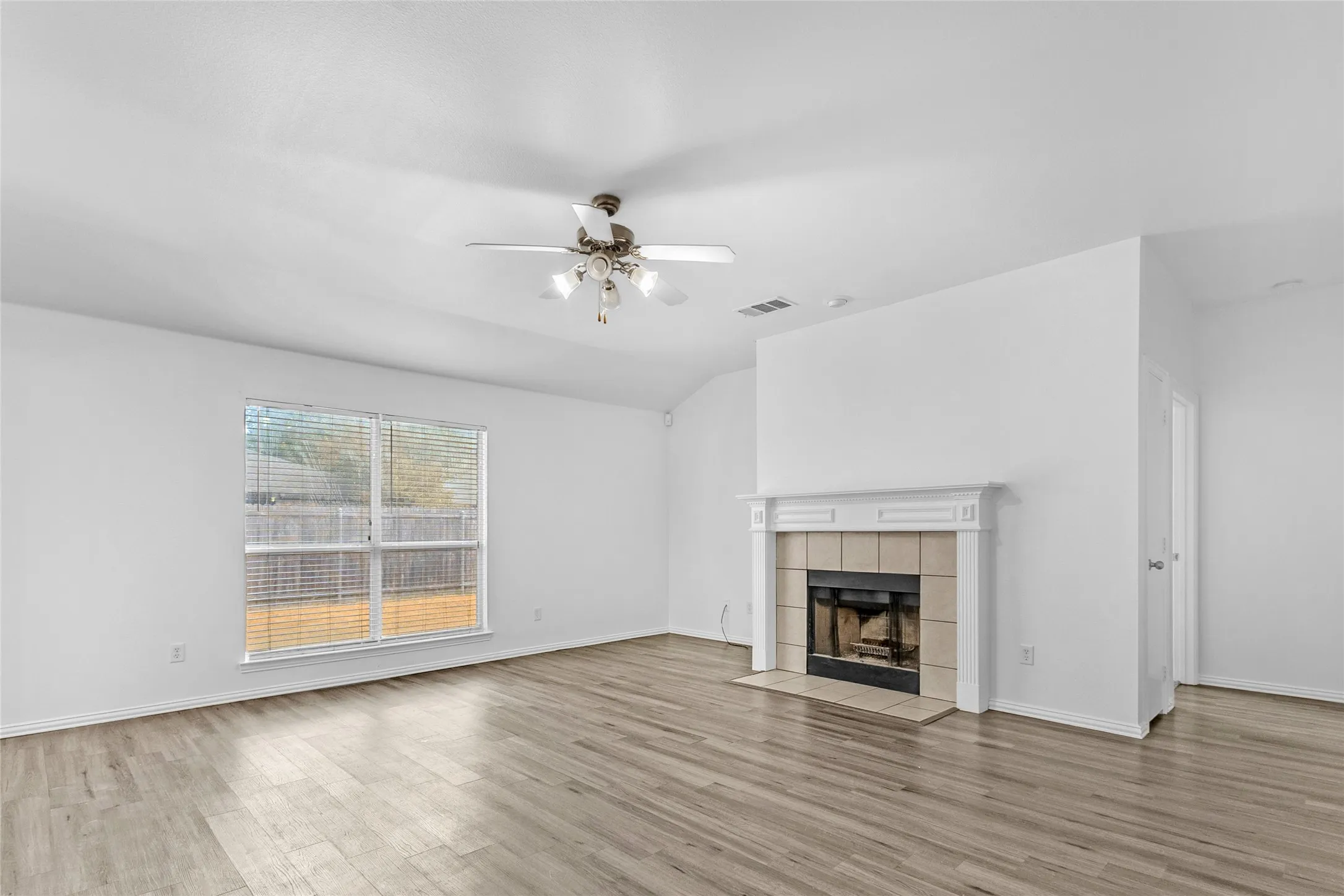Living room with wood-burning fireplace, tile surround, ceiling fan, and a window to the backyard