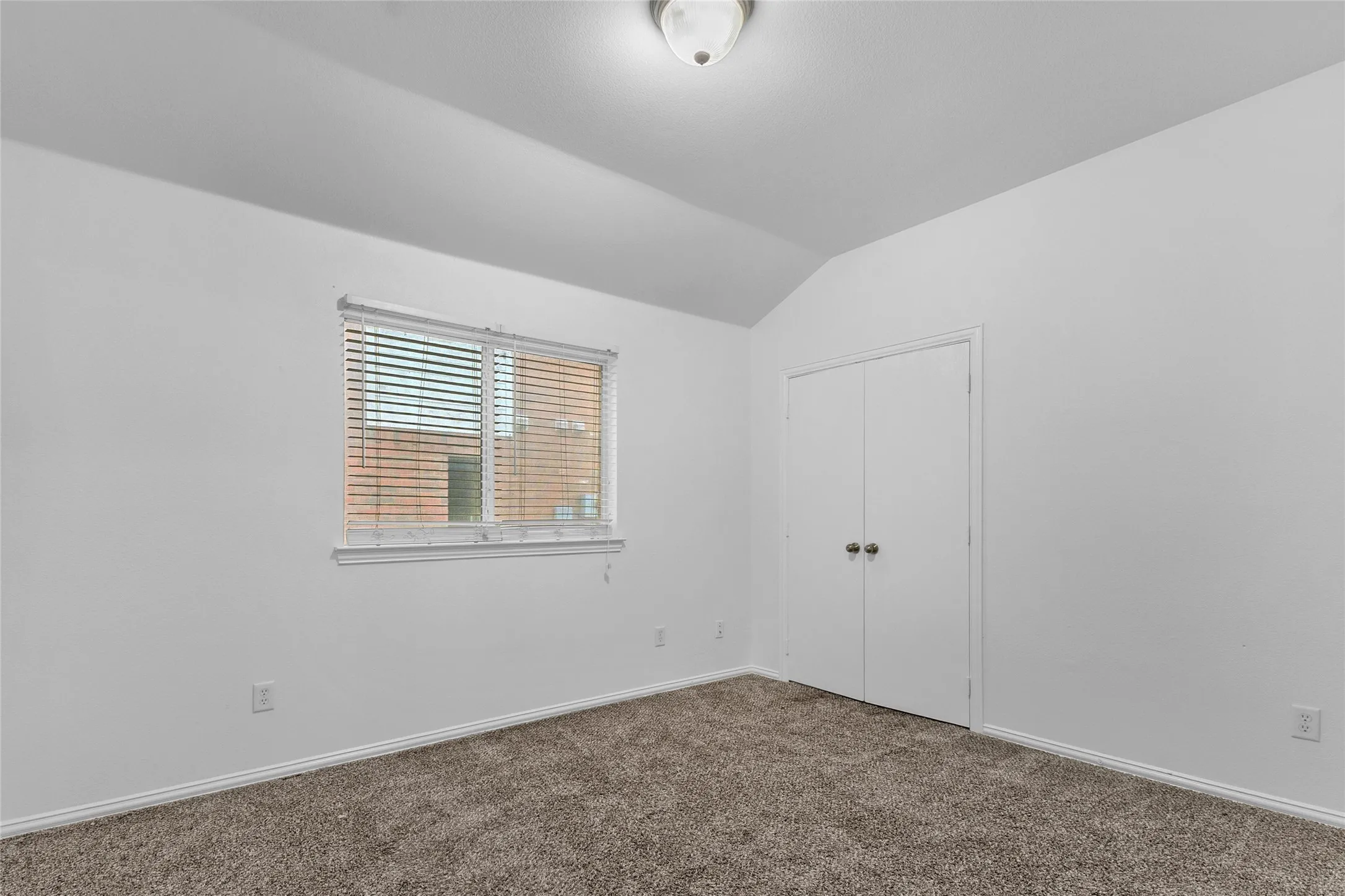 Carpeted secondary bedroom with vaulted ceiling and a double-door closet