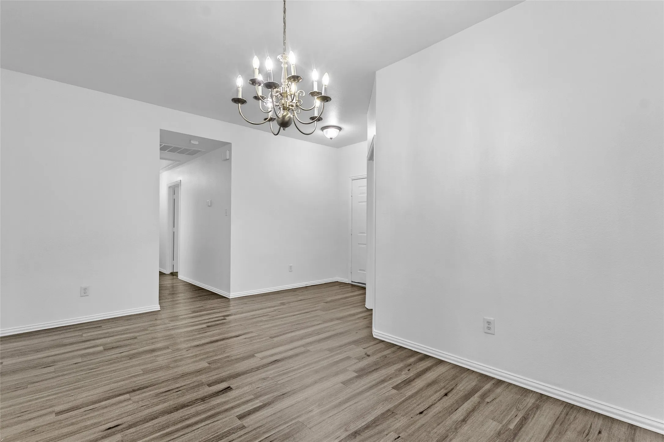 Dining room with chandelier and wood-look floors leading to the hallway and bedrooms