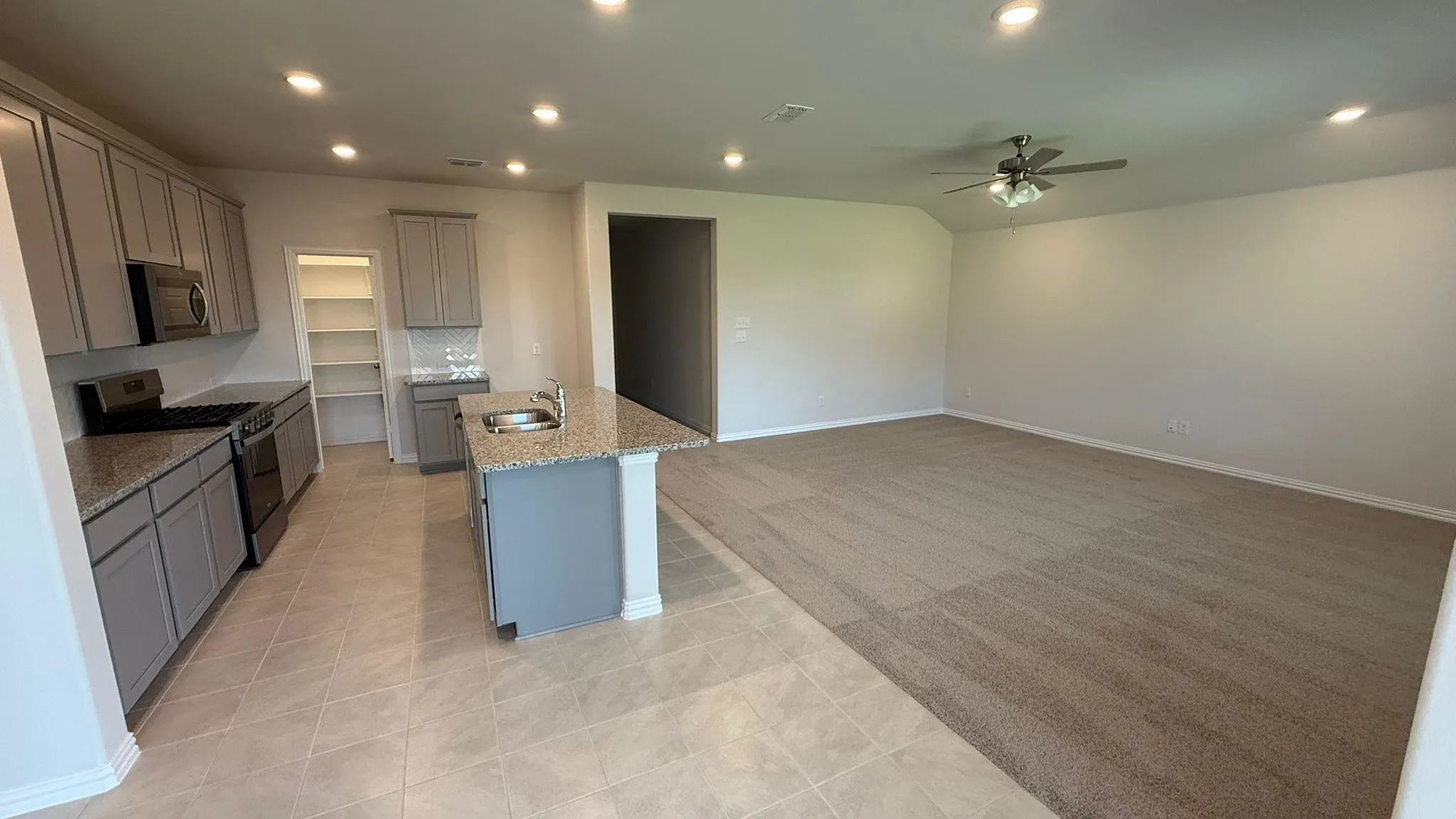 Kitchen island with integrated sink, granite countertops, tile flooring, recessed lighting, and a ceiling fan