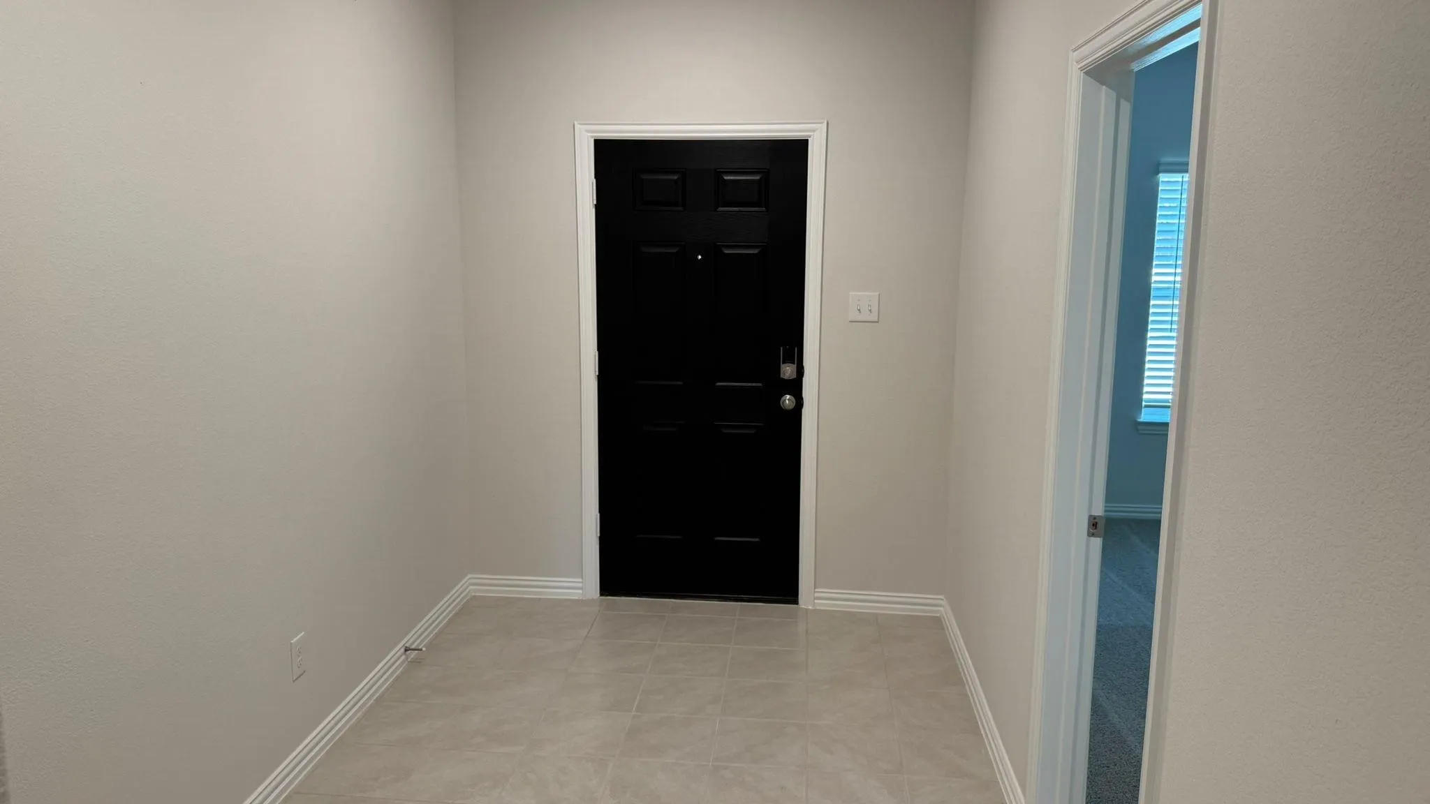 Black paneled door with polished hardware and light tile flooring