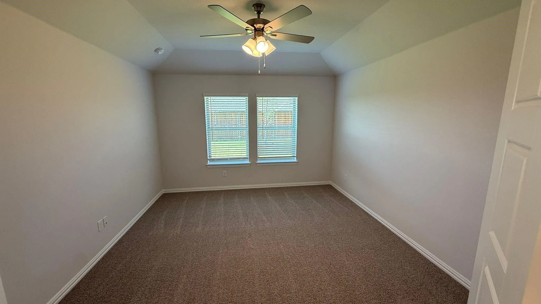 Tray ceiling with a ceiling fan light fixture, two windows with blinds, and neutral carpeting