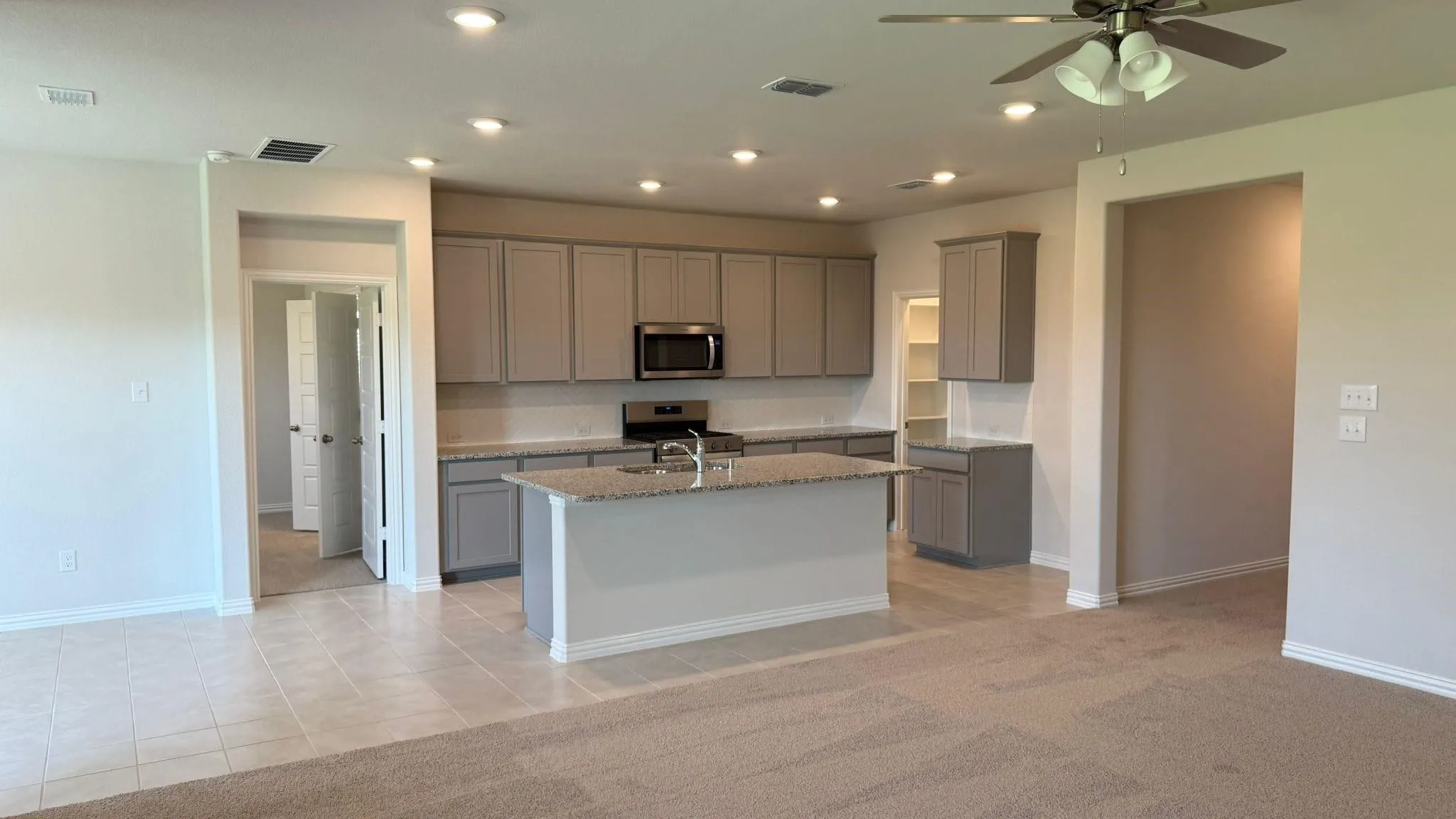 Open-concept kitchen featuring an island with a sink, stainless steel microwave, gray cabinetry, and recessed lighting