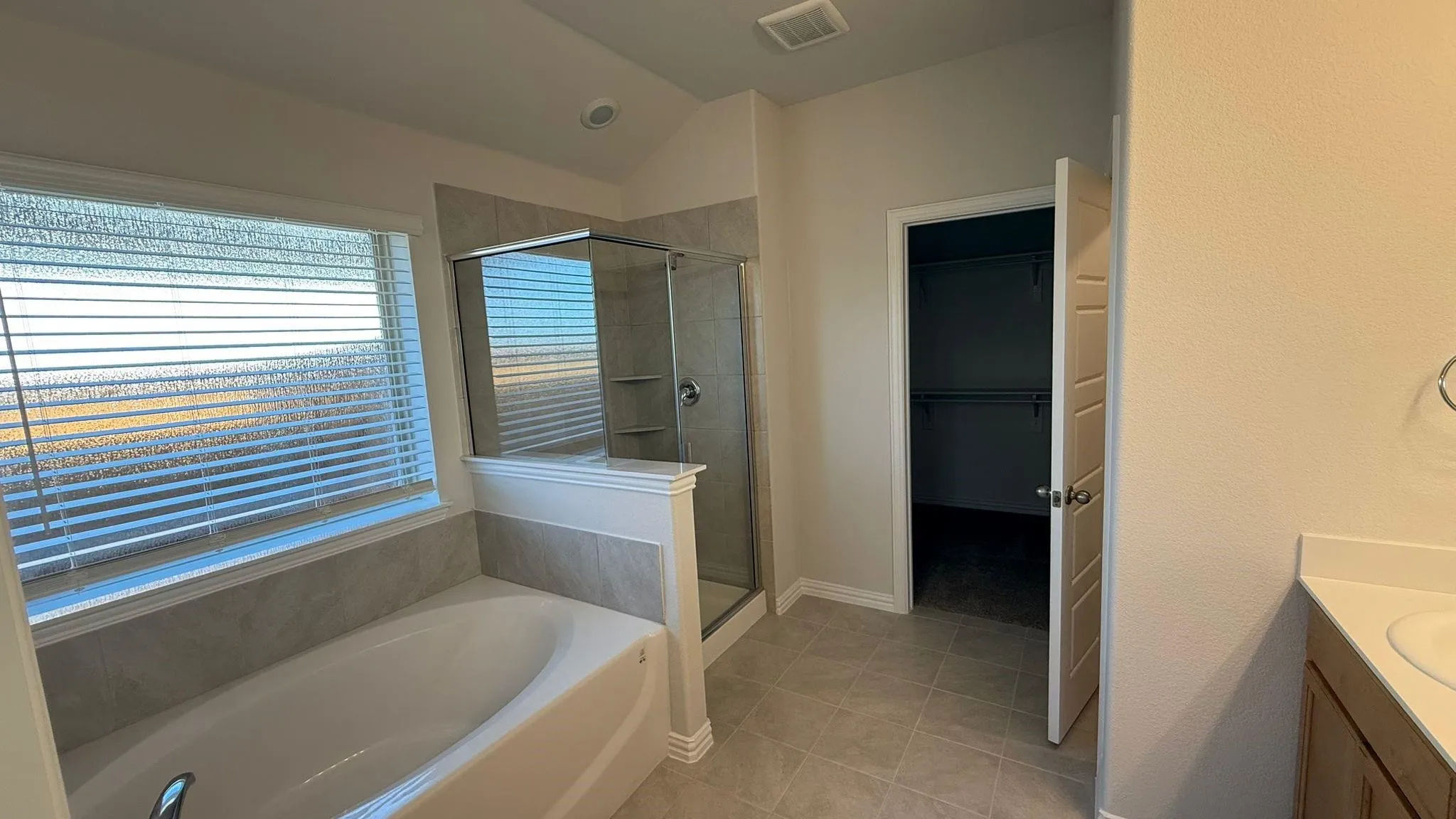 White soaking tub with tiled surround, glass-enclosed shower, and built-in closet storage