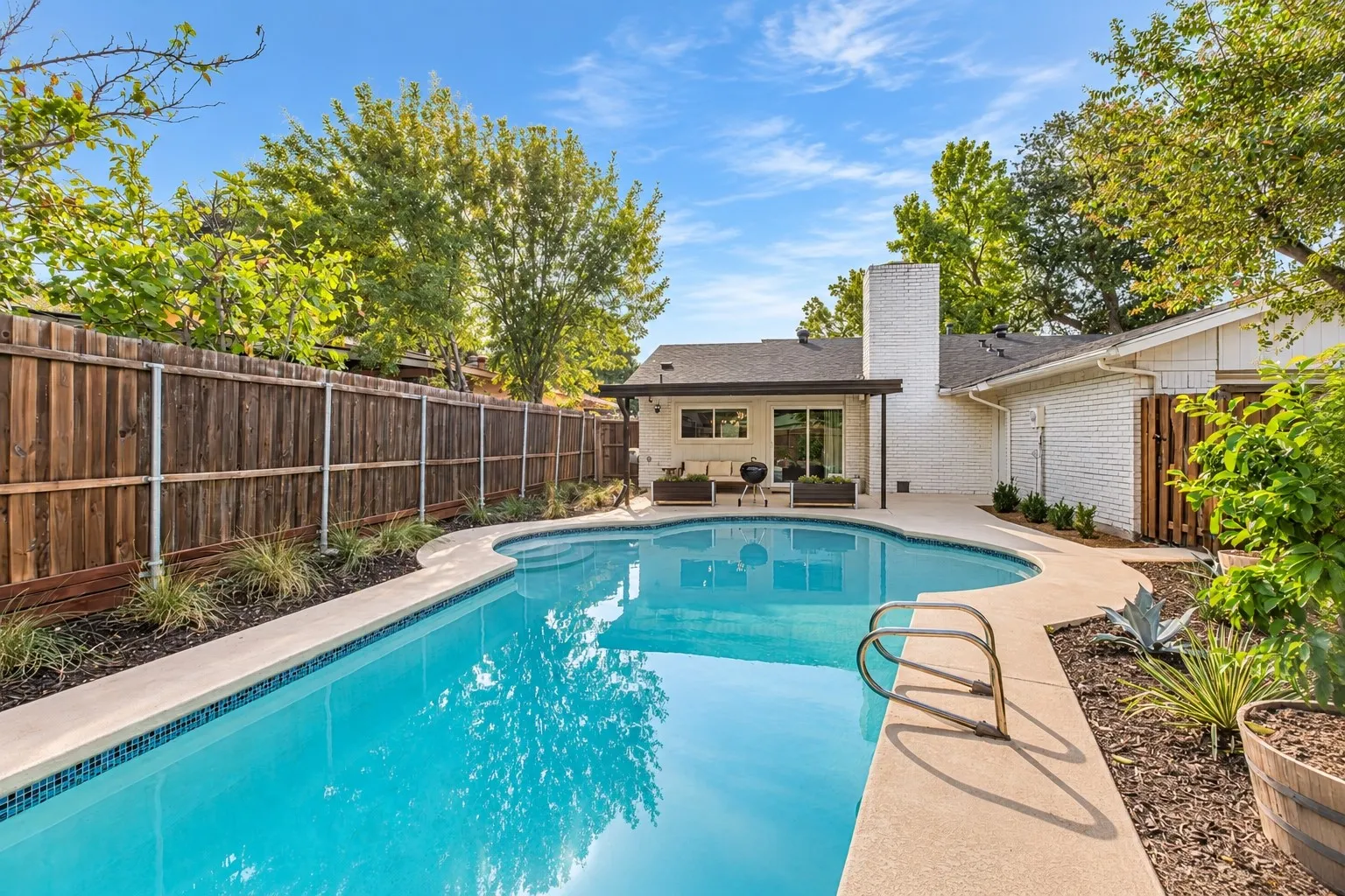 Freeform swimming pool with integrated steps, concrete decking, and mature landscaping