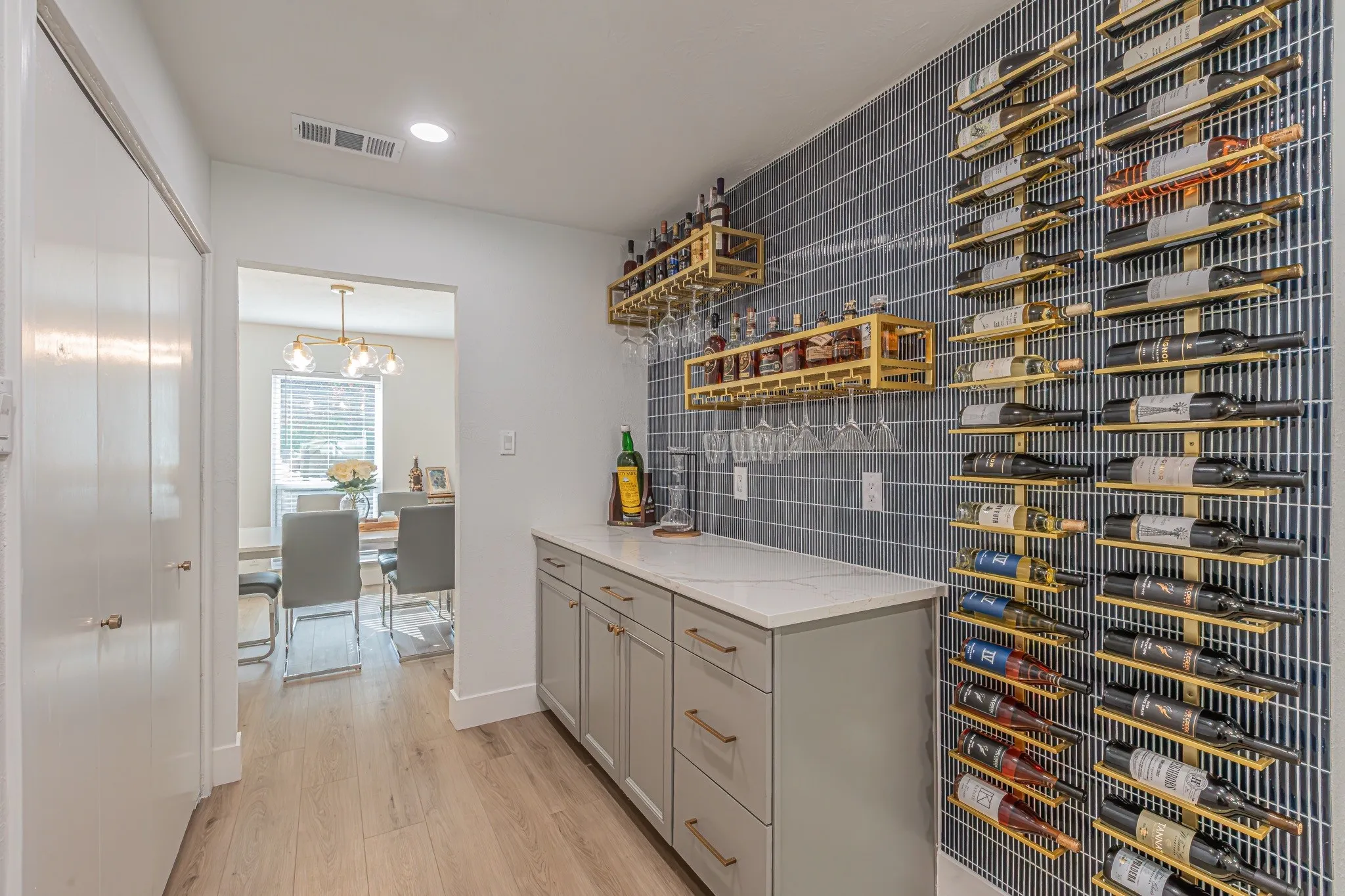 Built-in beverage bar with light gray cabinetry, a white countertop, and a tiled accent wall featuring horizontal wine racks
