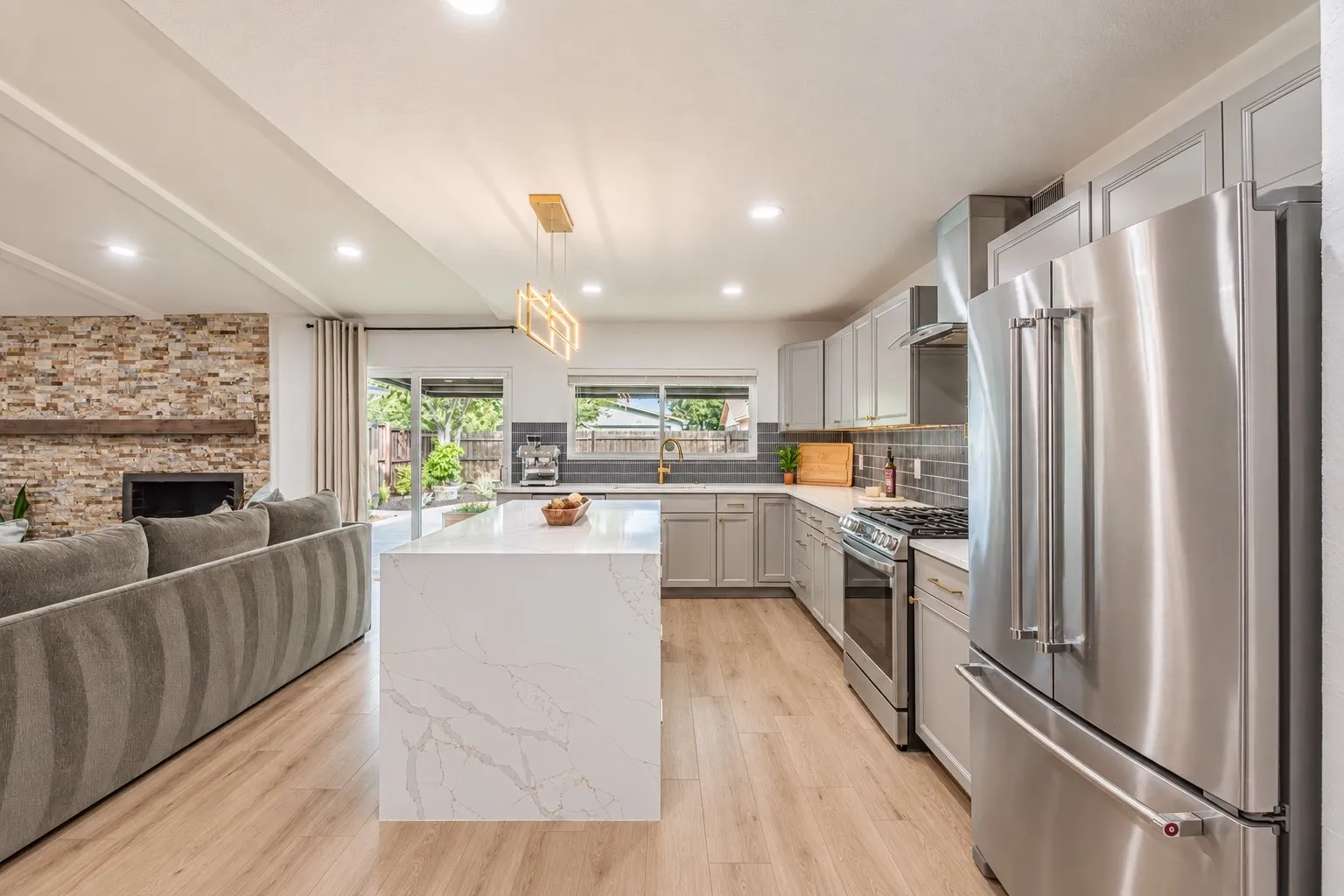 Open-concept living space with wood-finish flooring, a stone accent wall, and a built-in fireplace