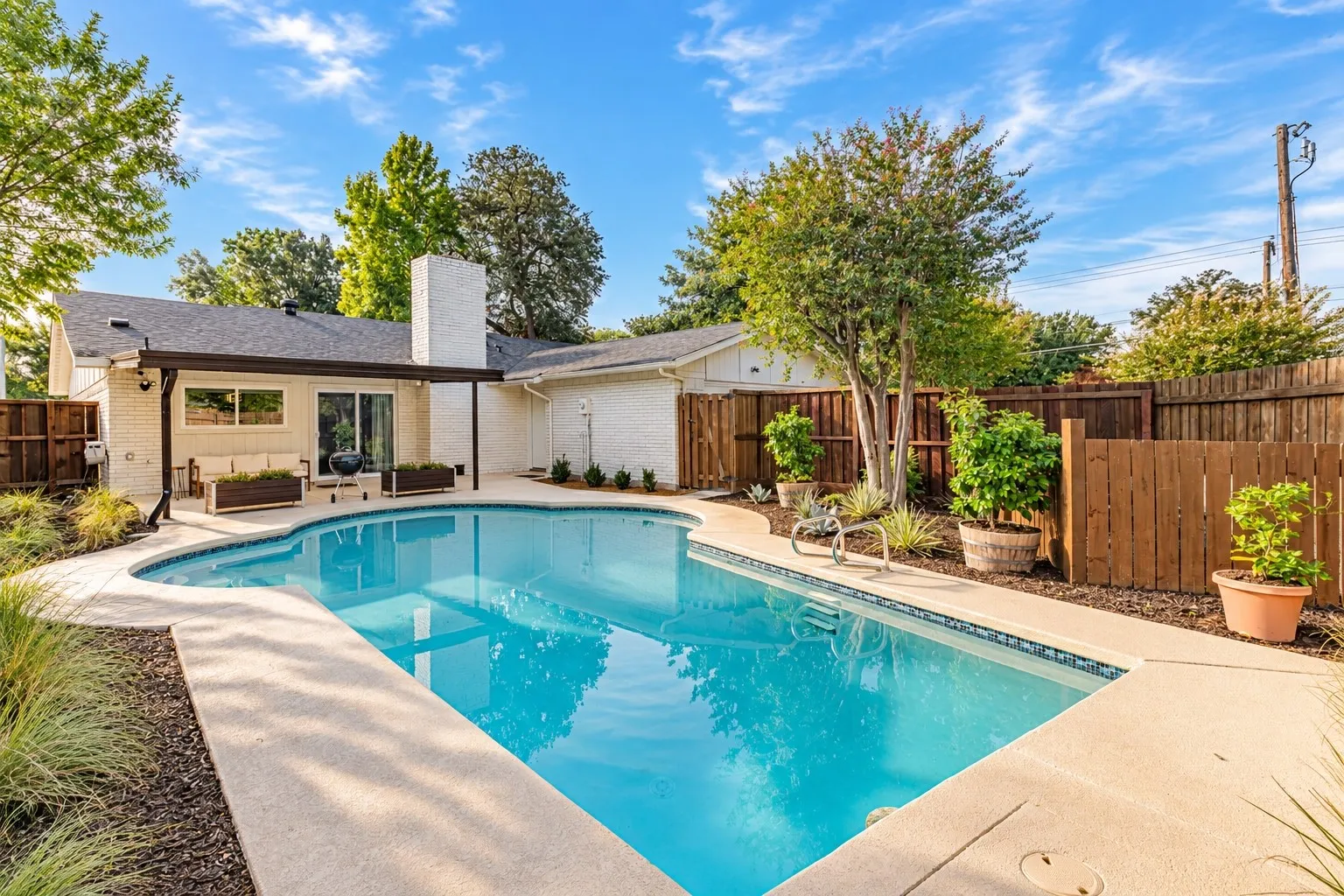 Backyard featuring an inground swimming pool, concrete decking, wood fencing, and a covered patio with a sliding glass door