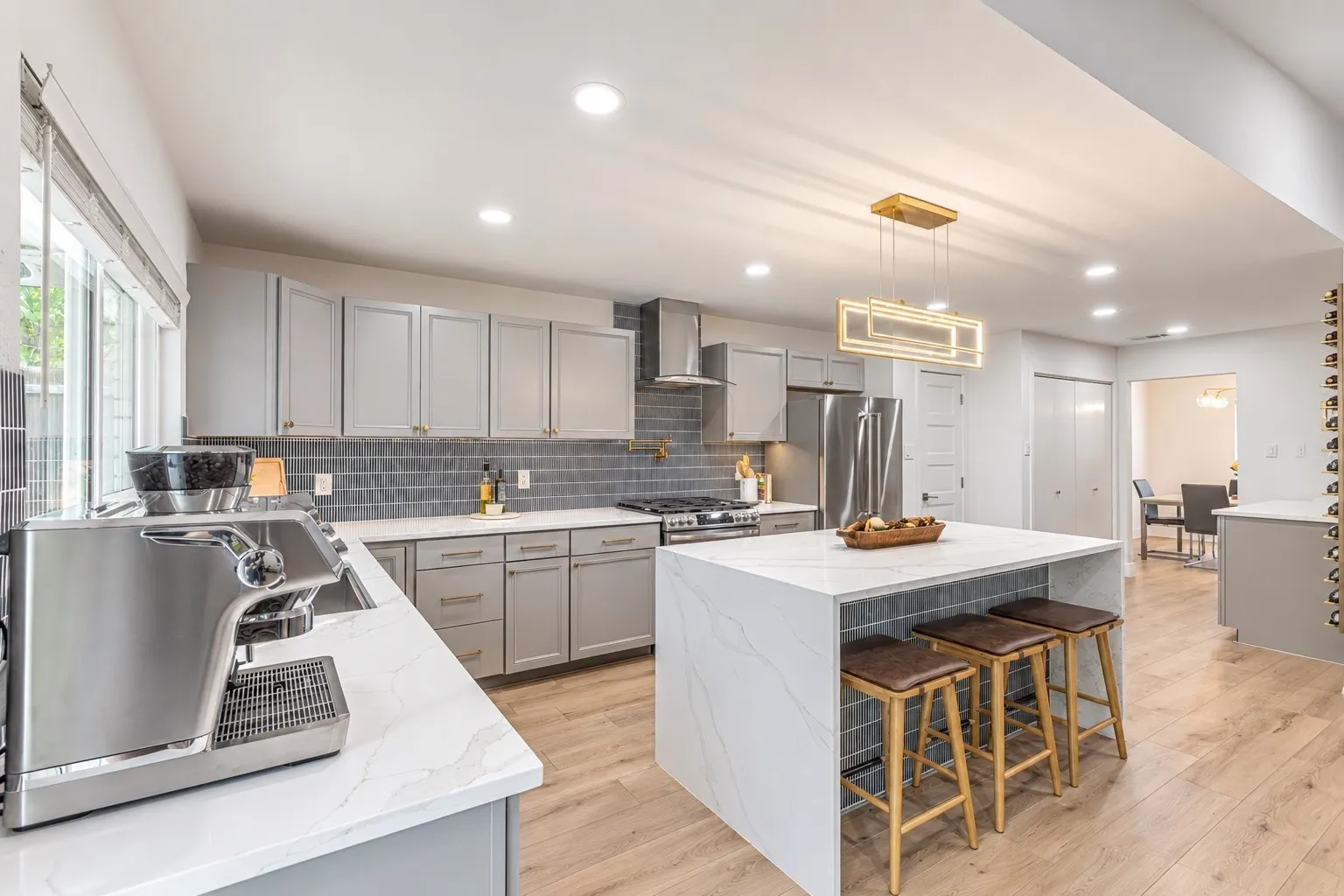 Gourmet kitchen with light gray cabinetry, white quartz countertops, full subway tile backsplash, and wood-finish flooring