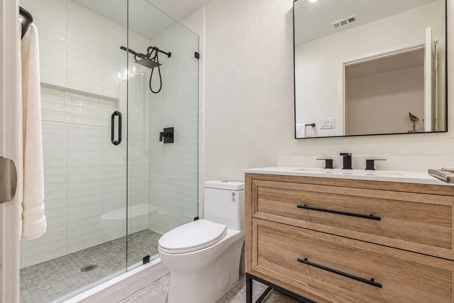 Glass-enclosed shower with white subway tile, a recessed niche, and a matte black rainfall showerhead