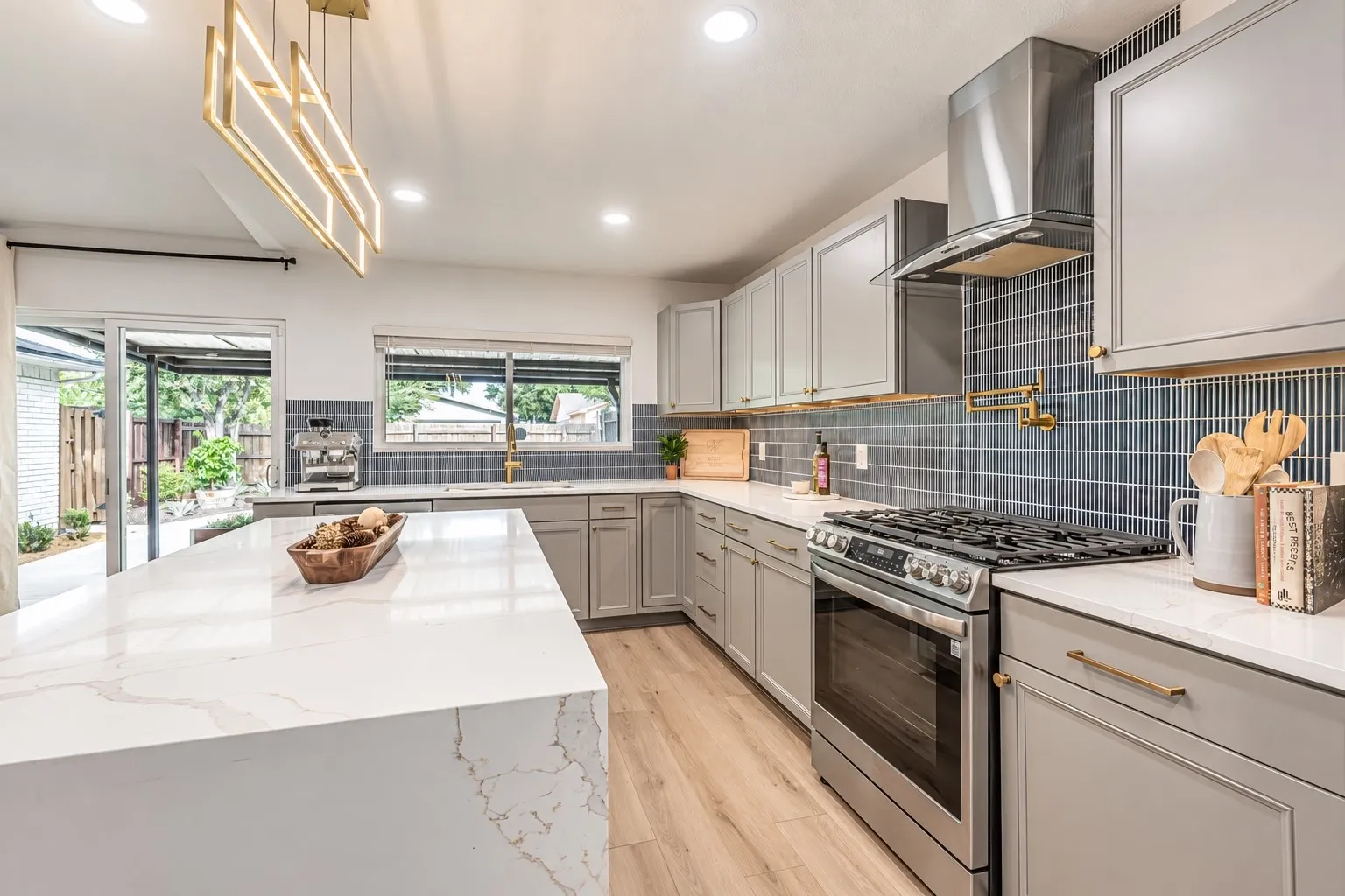 Kitchen featuring an expansive island with a waterfall countertop, wood-finish flooring, stainless steel appliances, and a tile backsplash