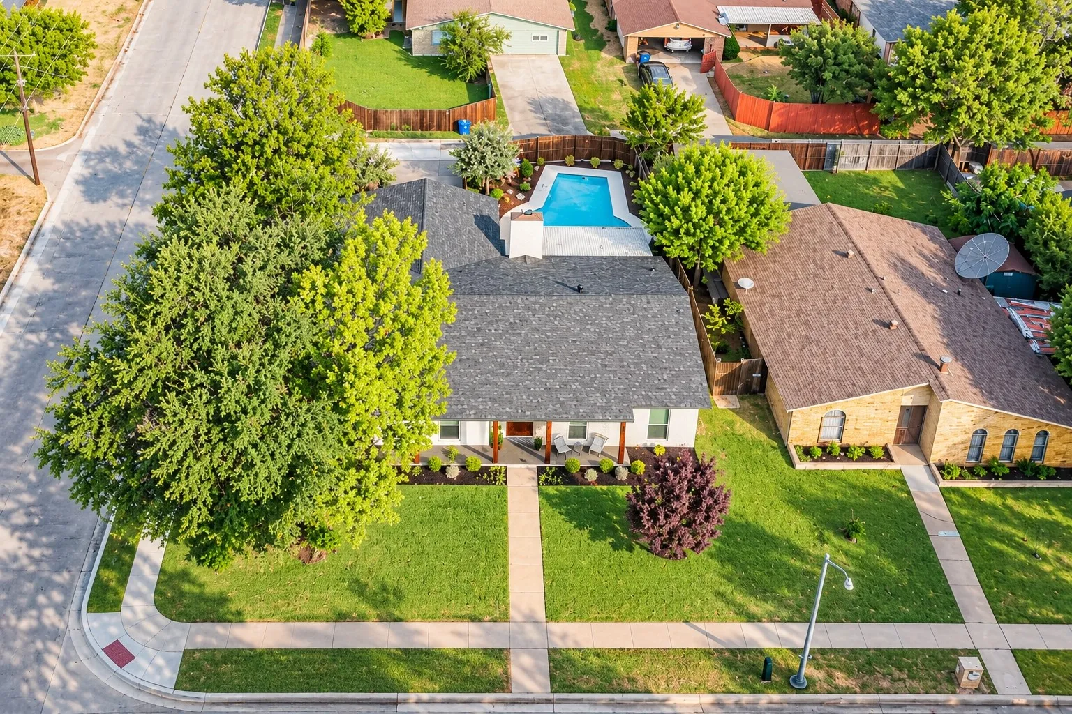 Manicured front lawn with mature trees, established landscaping, and a paved walkway