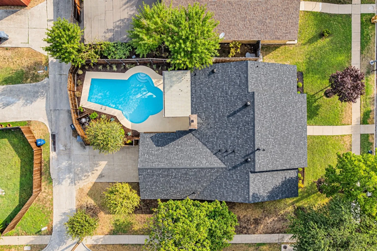 Shingled roof, paved driveways, a fence-enclosed pool, and established landscaping