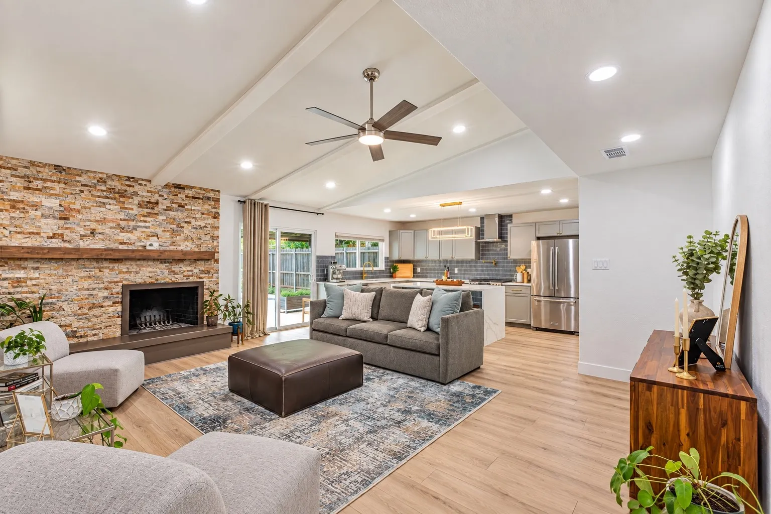 Vaulted ceiling with recessed lighting and ceiling fan, stone-clad fireplace with wood mantel, wood-finish flooring, and sliding glass door to exterior