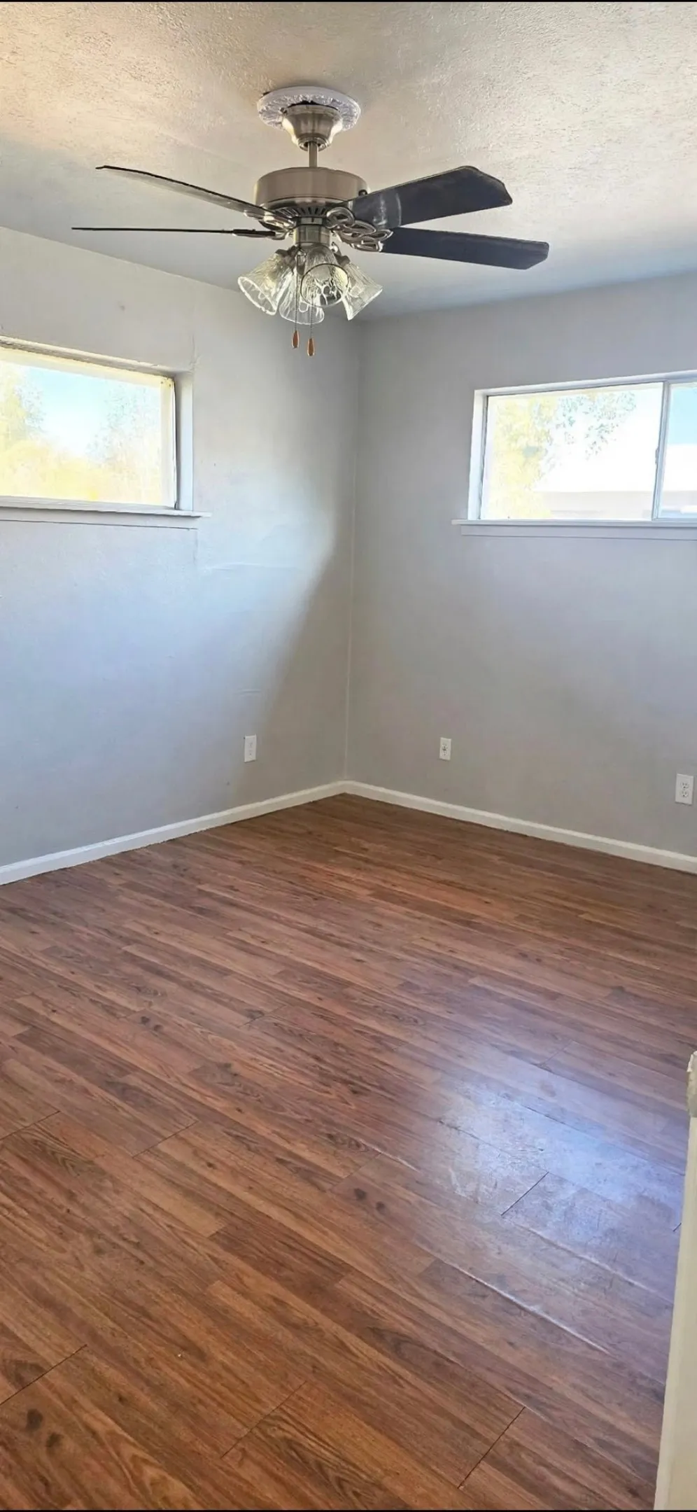 Wood-finish flooring with light-colored walls, two horizontal windows, and a ceiling fan with integrated lighting