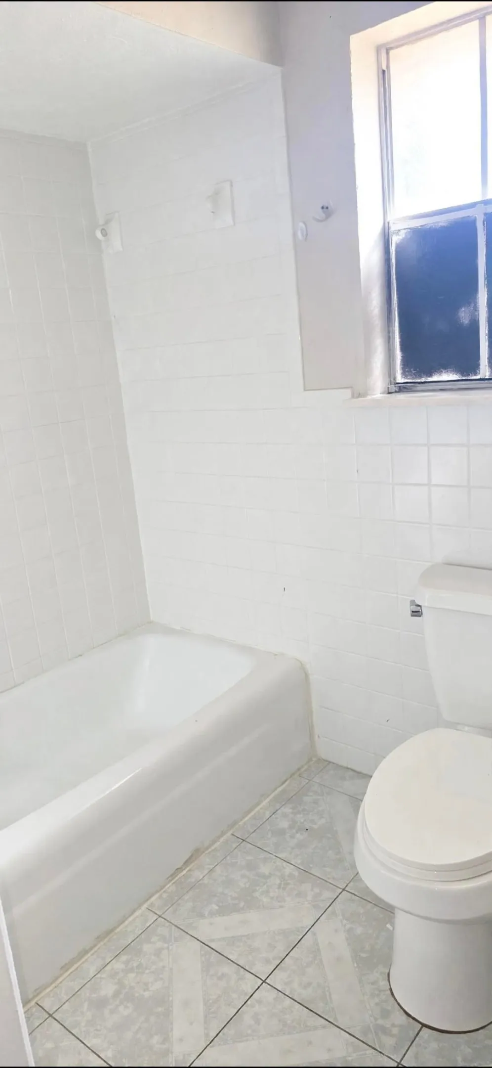 White tile walls, white bathtub, white toilet, and patterned floor tile